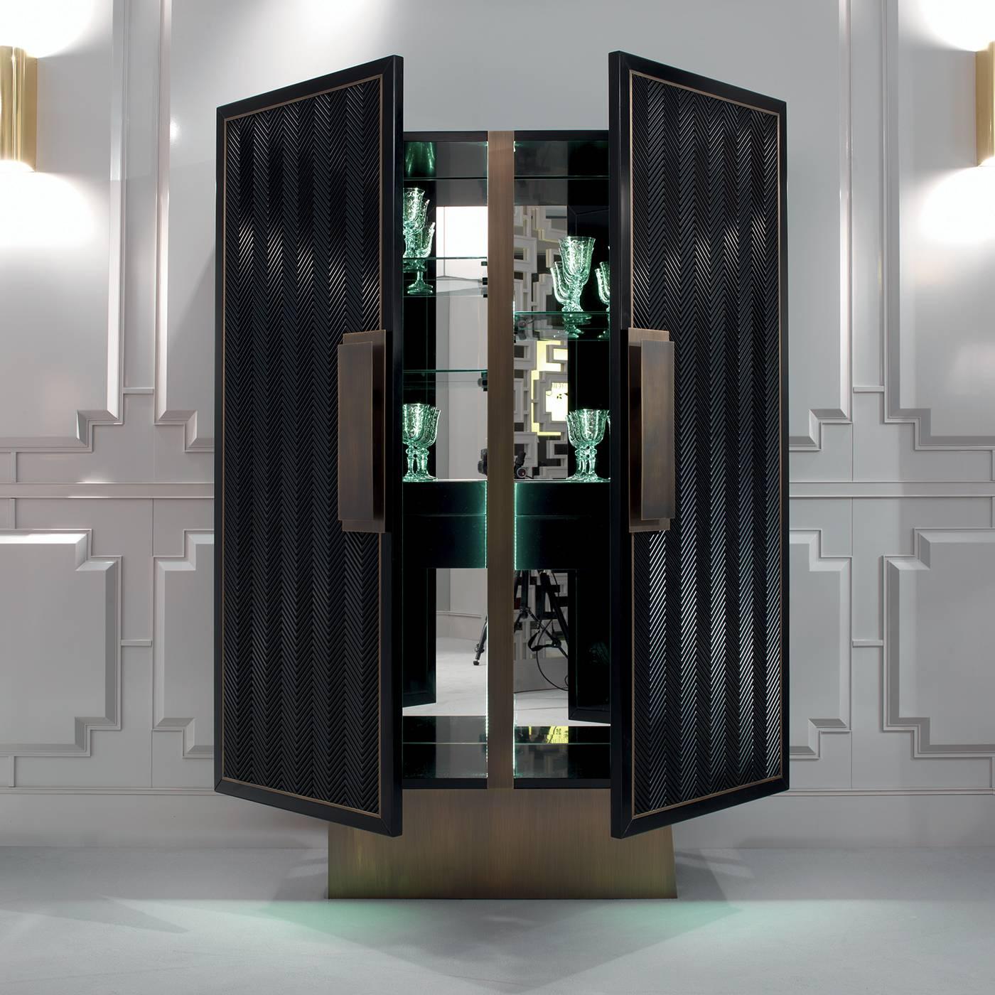 This superb bar cabinet is inspired by the geometric style and lavish charm of Art Deco and it features a thick plinth base in satin-finished brass supporting a rectangular Silhouette made in wood with a black lacquered finish. The two front doors