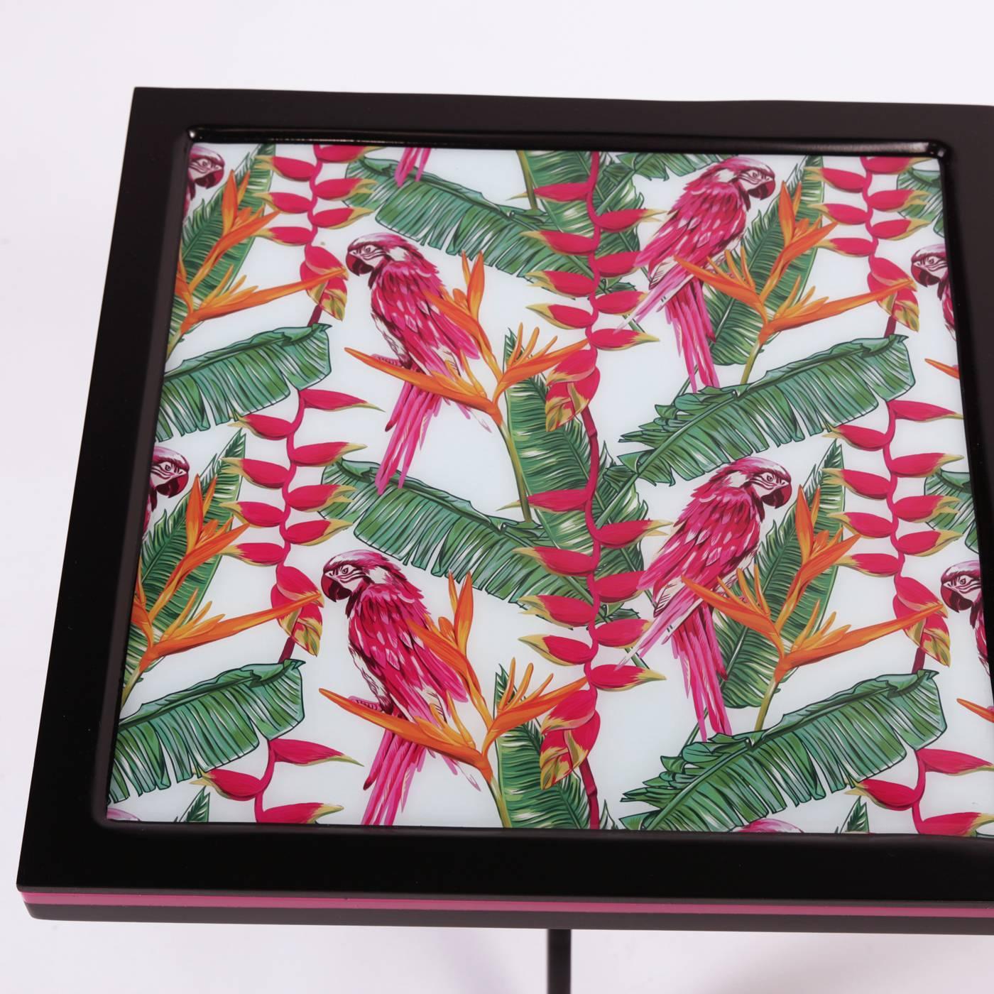 This striking side table will add a touch of color to any room, thanks to the exquisite cover of its top depicting a series of green palms and bright red parrots. A red accent outlines the squared edges of the top that is supported by a three-legged