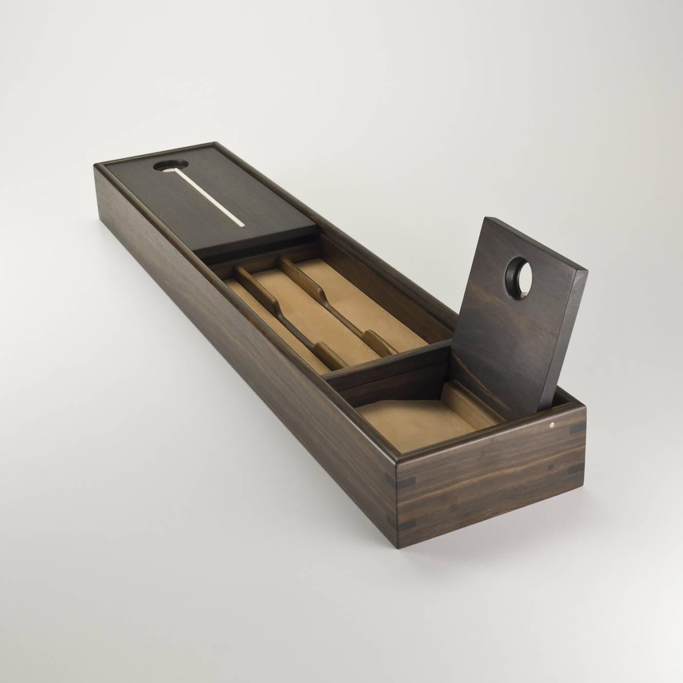 This elegant pen tray in ebony wood with horn accents in contrasting color has a mini-shutter that slides to cover its content and it features a side compartment for cellphones with a pivot closing. The interior is lined in nubuck leather. 

