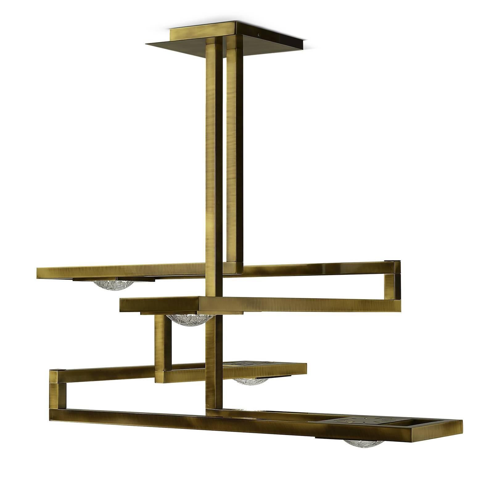 This exquisite lamp was entirely made of brass. It is attached to the ceiling through a square base, from which two vertical elements hang, creating a Minimalist structure with four arms that create a square Silhouette, hanging at different heights