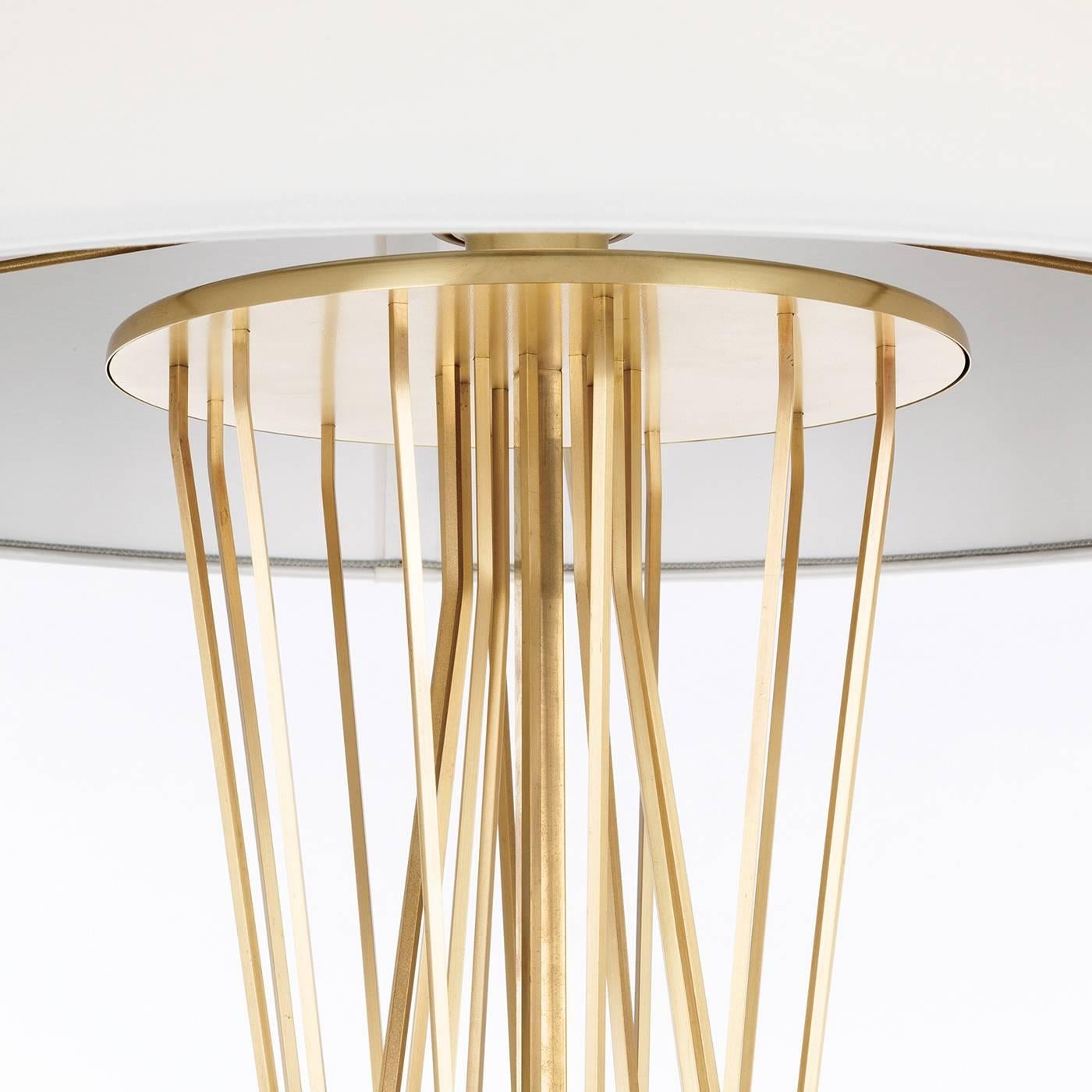 This magnificent table lamp is part of the Saba collection and features a square base in bronzed brass supporting a sculptural vertical element made up of several brass rods, bent at different angles that intersect to create a dynamic and airy