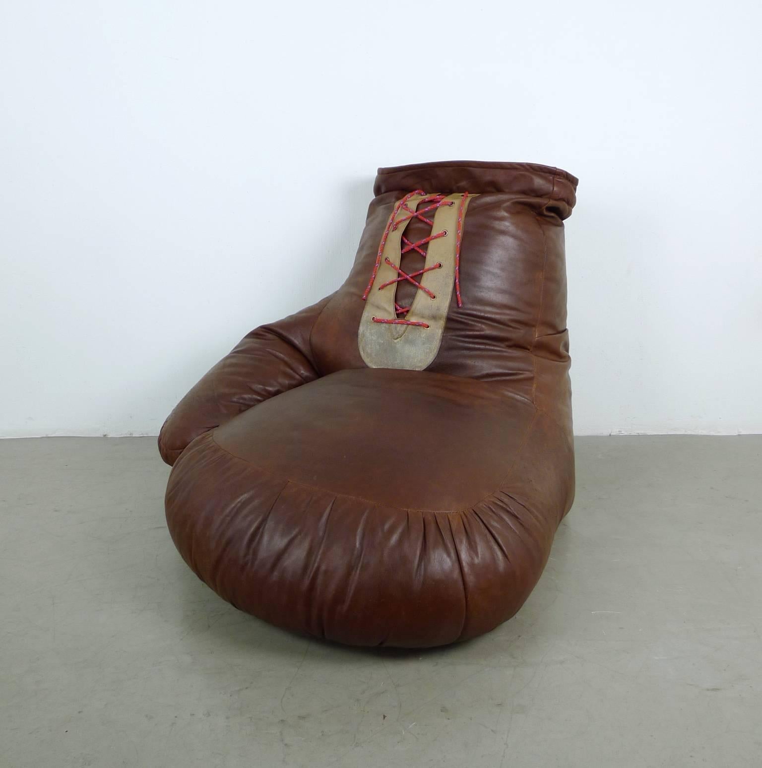 This saddle leather seat in the shape of a boxing glove was designed by Ueli bergere in the 1970s for De Sede from Switzerland. 
All seams are intact, the filling is plump and the leather is soft and supple. The leather of the cording is a little
