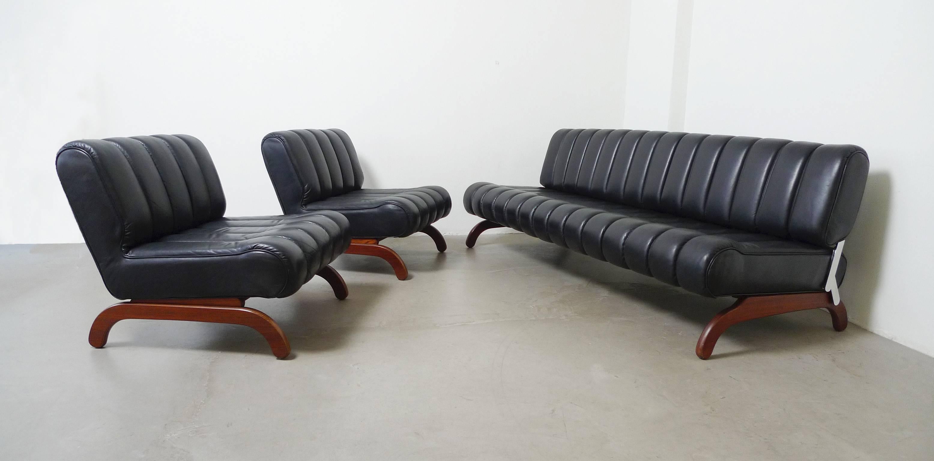 Very rare and extraordinary streamlined seating group with sofa bed and two easy chairs. Upholstery and black leather cover is subdivided through longish quilted seams. The base has the form of an elegant curved bow and is made of wood. The back