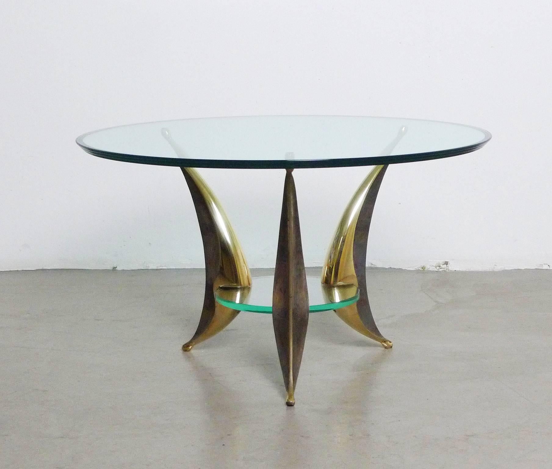 Significant Italian coffee table with two plates and three massive brass feet from the 1950s. The skillful design of the elegant swung brass feet, gripping and bearing the glass, reminds on the work of a sculptor. Each case leg has a polished