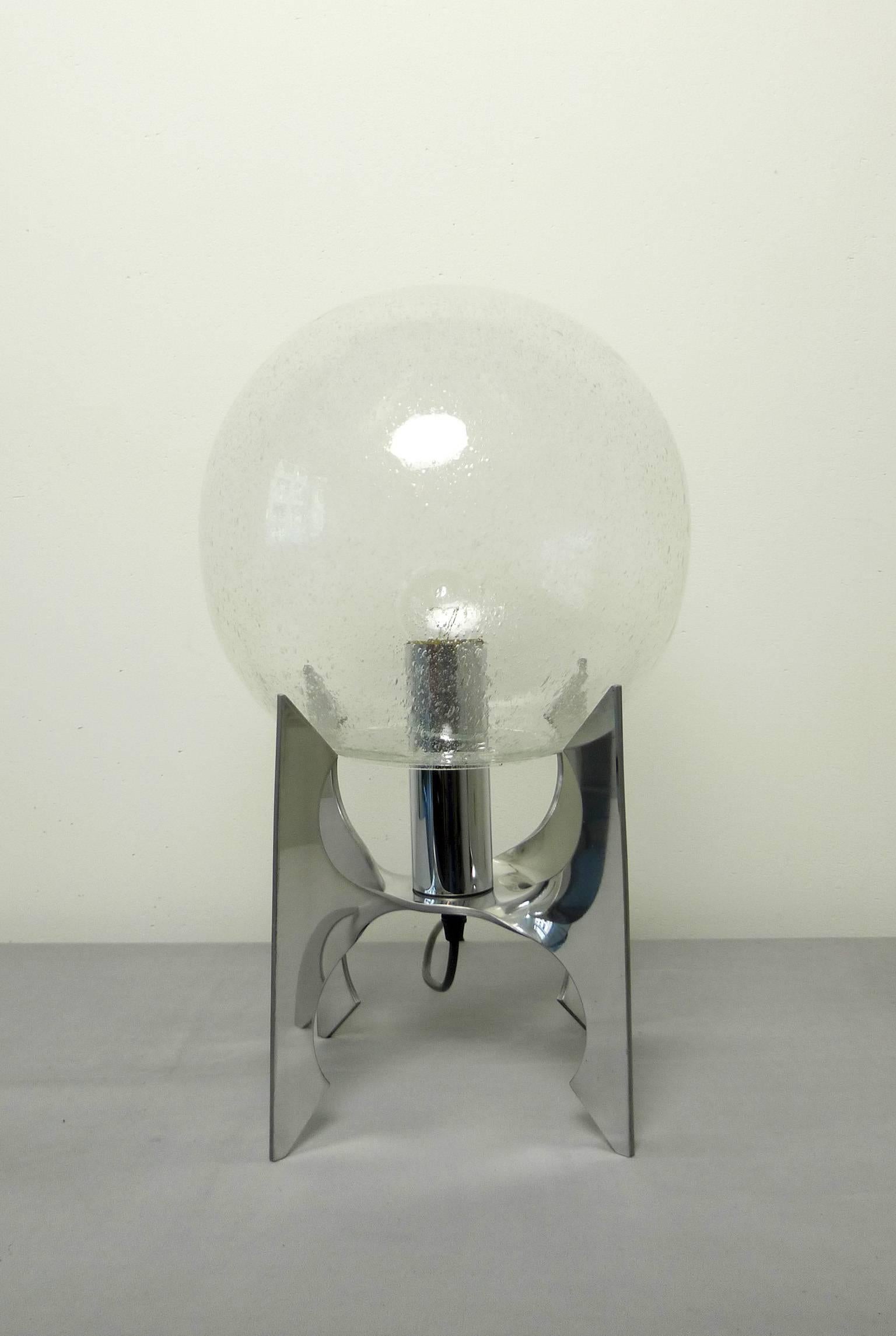 German space table lamp in the shape of the Apollo rocket from the 1970s. The polished aluminium base holds a large glass globe with air bubbles inside. These bubbles throw a Milky Way shadow to the wall.
This Space Age lamp has one E 27 bulb