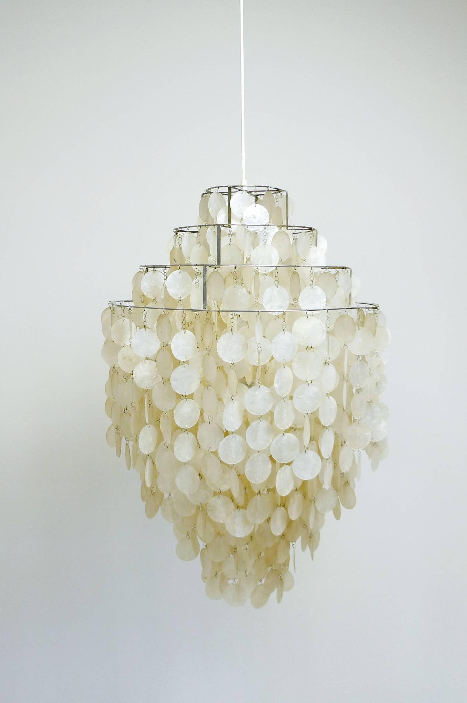 Impressive sea shell chandelier from the first production series 1964 by Verner Panton for the Swiss manufacturer J. Luber Ag.
A large amount of sea shells hanging in tiers from four chromed rings. Two E27 bulbs illuminate the glimmering