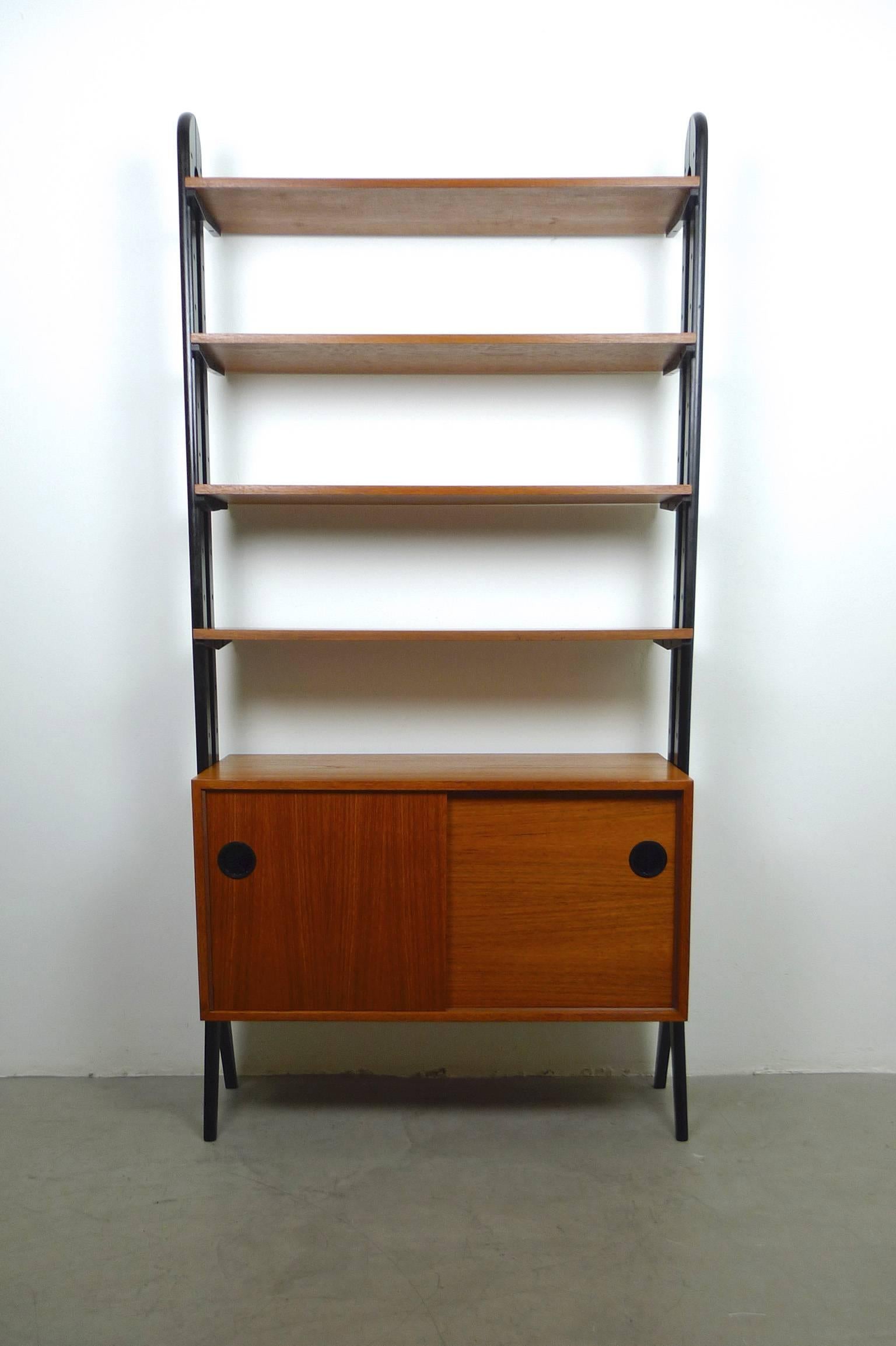 Rare teak wood bookshelf with elegant swung ladders, which are lacquered in black. It has four boards and a box with two sliding doors. This freestanding model can also be used as a room divider. Also the rear side is elaborated. The bookcase is in