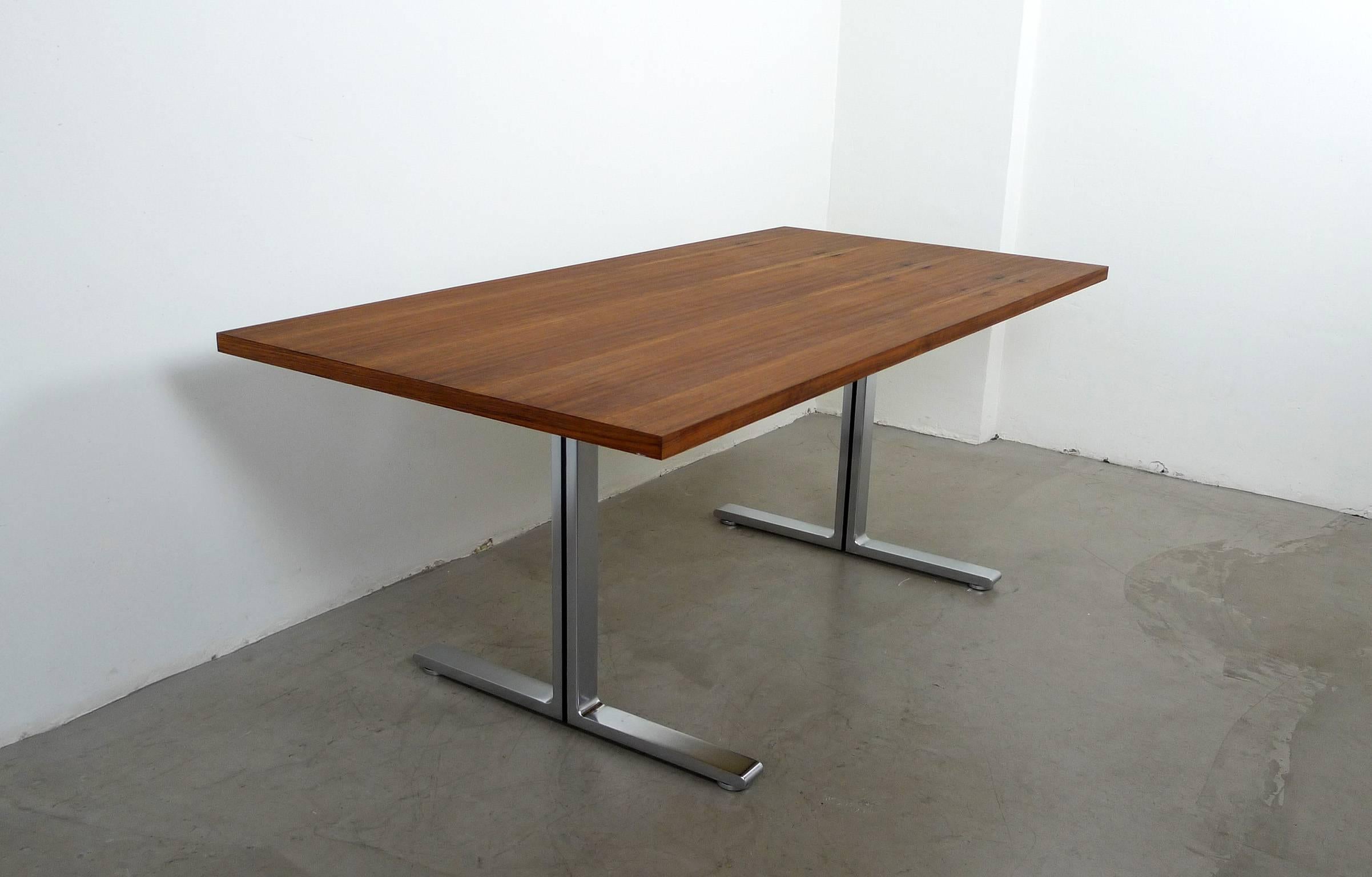 This walnut table from the Alpha series was produced by German manufacturer Walter Knoll in the 1970s. It can be used as a working or dining table. The table features a stabile polished steel base with four round adjustable feet to balance out