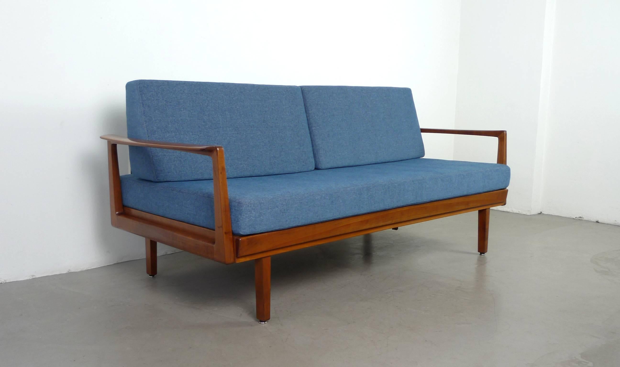 The German manufacturer Walter Knoll designed and produced this daybed in the 1950s. It has a walnut frame and a blue fabric cover.
By pulling out the left armrest one of the backrest cushions fills the gap for relaxing or sleeping. The extended