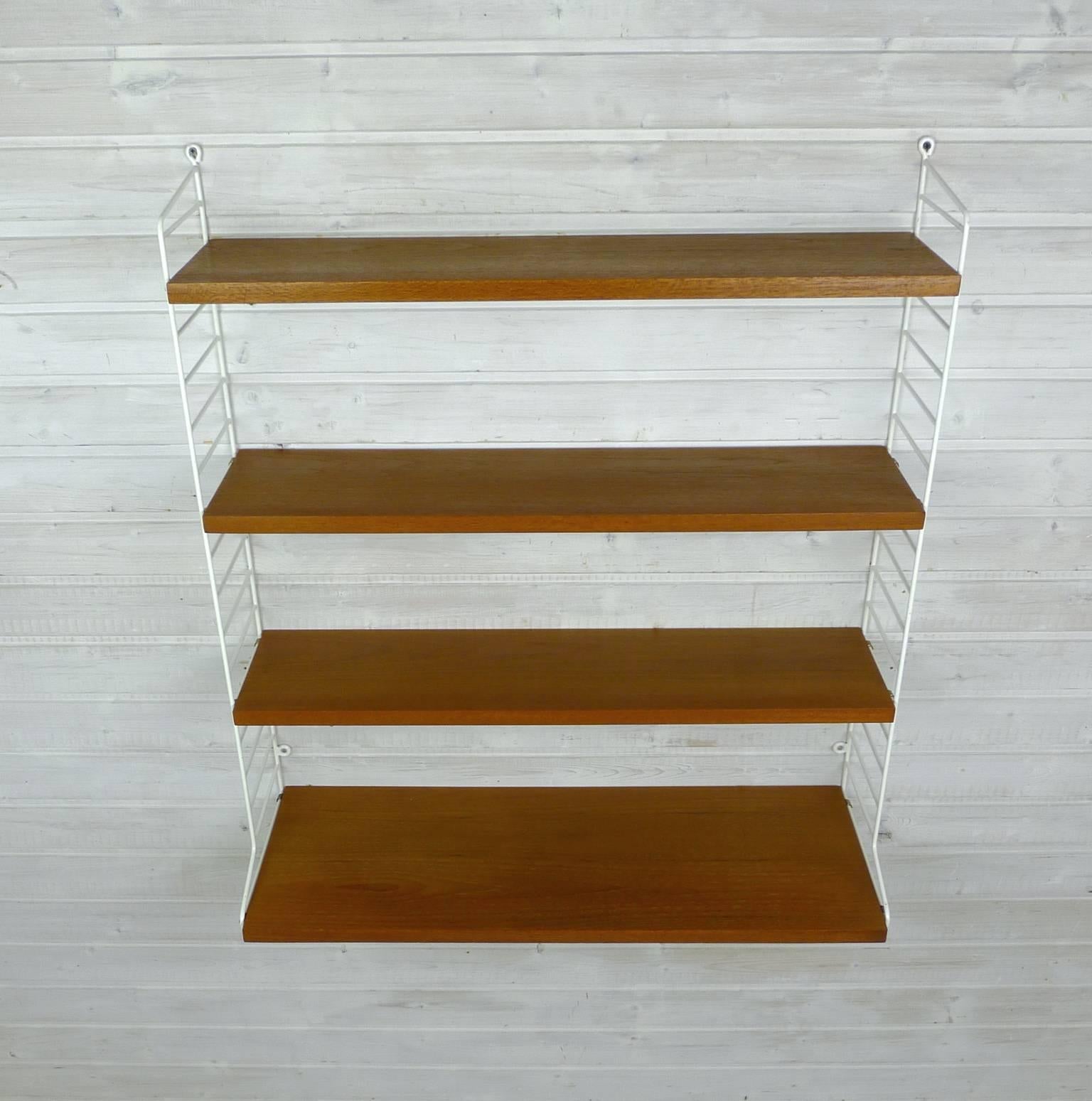 Nisse Strinning designed his famous shelving system in 1949. It was produced by his own operating String Design AB in Sweden. This wall shelf consists of two white coated ladders, three teak shelves with a depth of 20 cm, and a shelf with a depth of