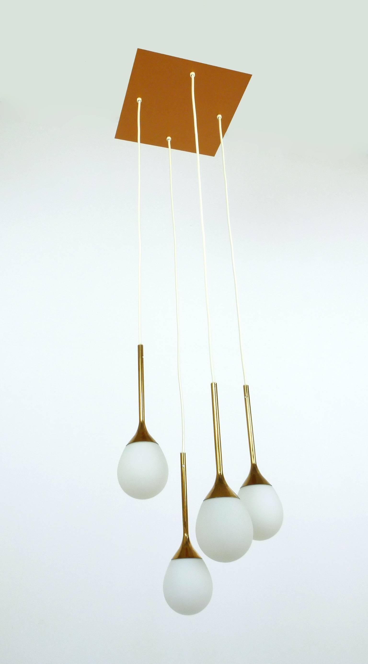 This cascading pendant was made by German manufacturer Staff Leuchten in the 1960s. The lamp features a square ceiling rose with four trumpet-shaped lights each hanging in different heights. The white round glass shades feature copper tops. Each