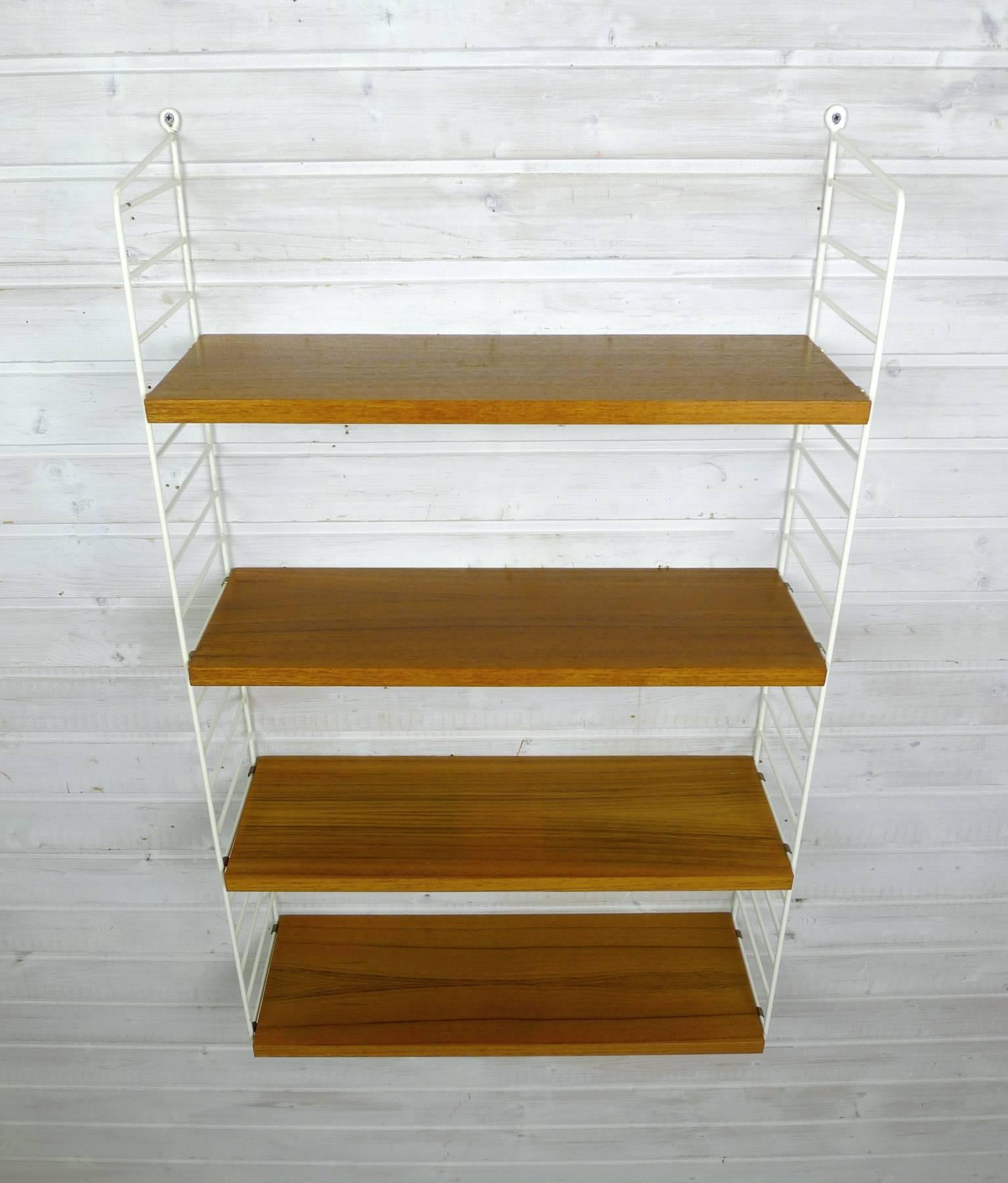 Nisse Strinning designed his famous shelf system in 1949. It was produced in his own company String Design AB in Sweden. 
This wall shelf consists of two white-coated ladders and four shelves in teak with a depth of 20 cm. The shelf is in a good