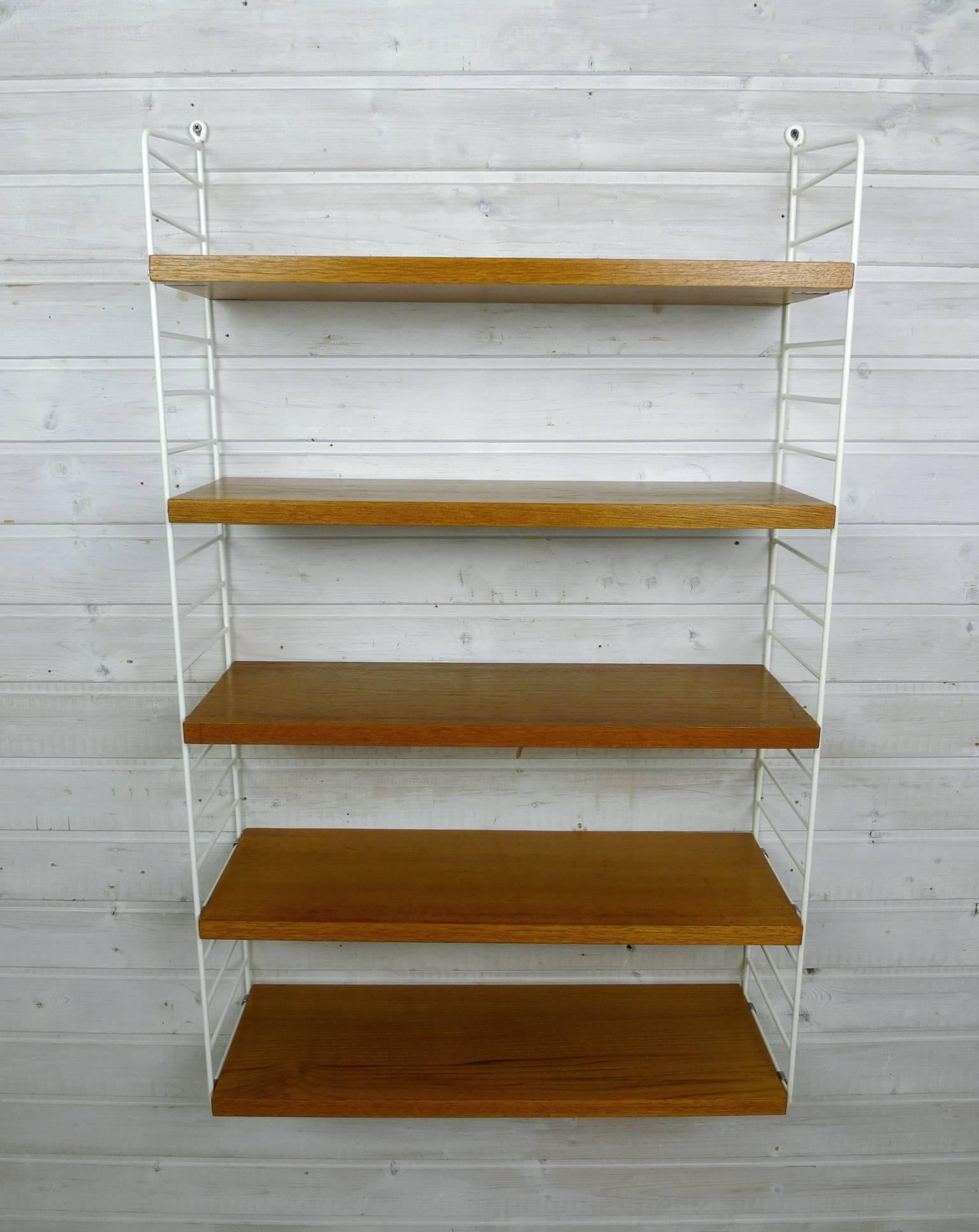 Nisse Strinning designed his famous shelf system in 1949. It was produced in his own company String Design AB in Sweden.
This wall shelf consists of two white-coated ladders and five shelves in teak with a depth of 20 cm. The shelf is in a good