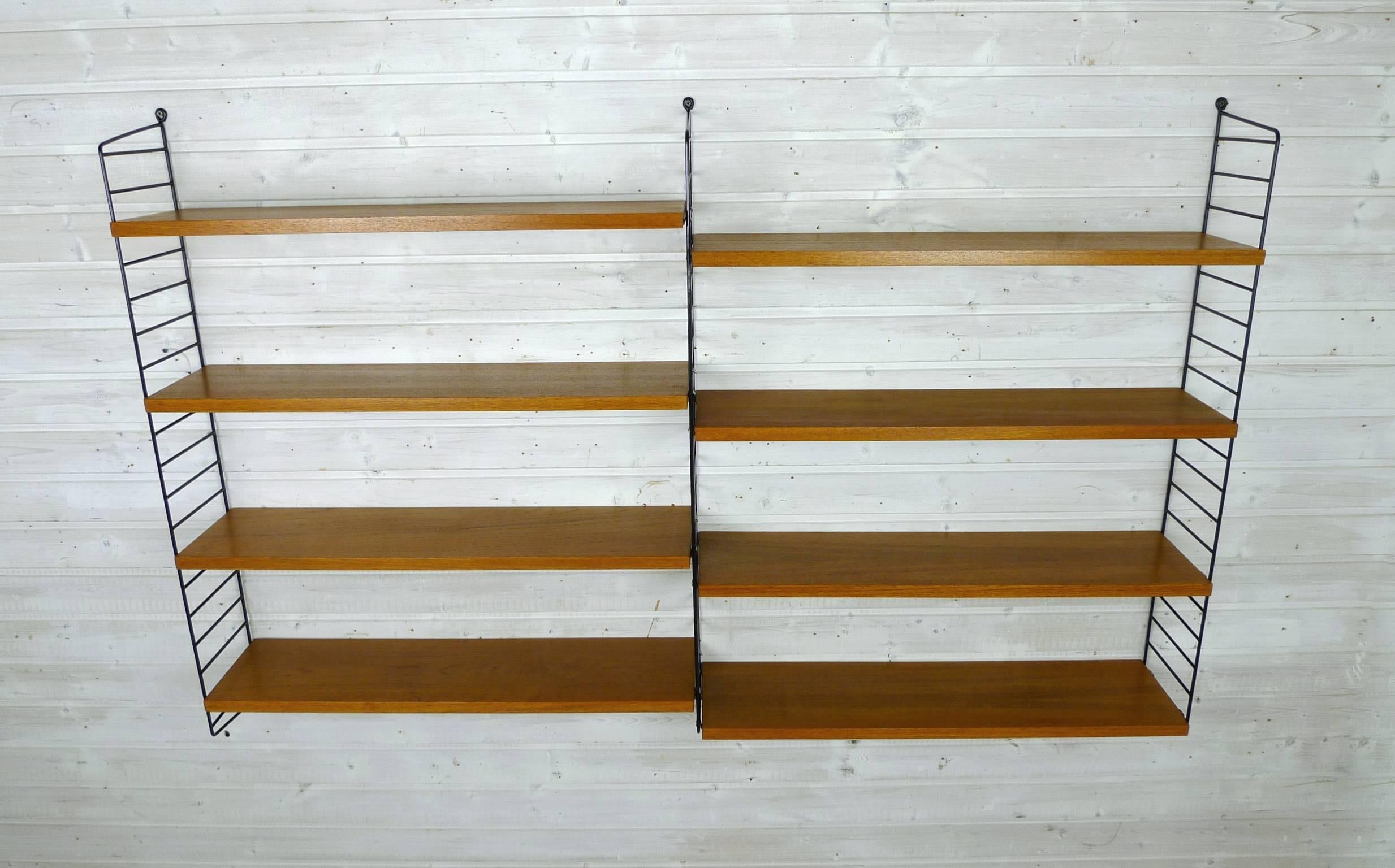 Nisse Strinning designed his famous shelf system in 1949. It was produced in his own company String Design AB in Sweden. 
This wall shelf consists of three black-coated ladders and eight shelves in teak with a depth of 20 cm. The shelf is in a good