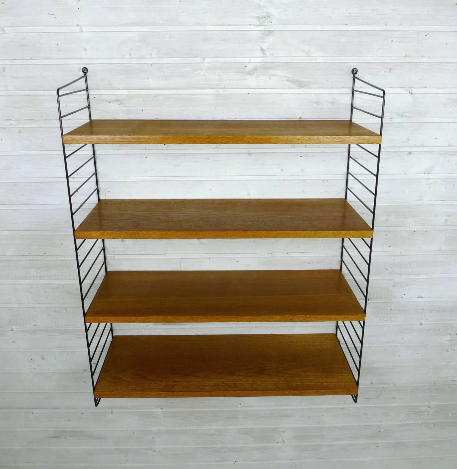 Nisse Strinning designed his famous shelf system in 1949. It was produced in his own company String Design AB in Sweden. 
This wall shelf consists of two black-coated ladders and four shelves in teak with a depth of 30 cm. The shelf is in a good