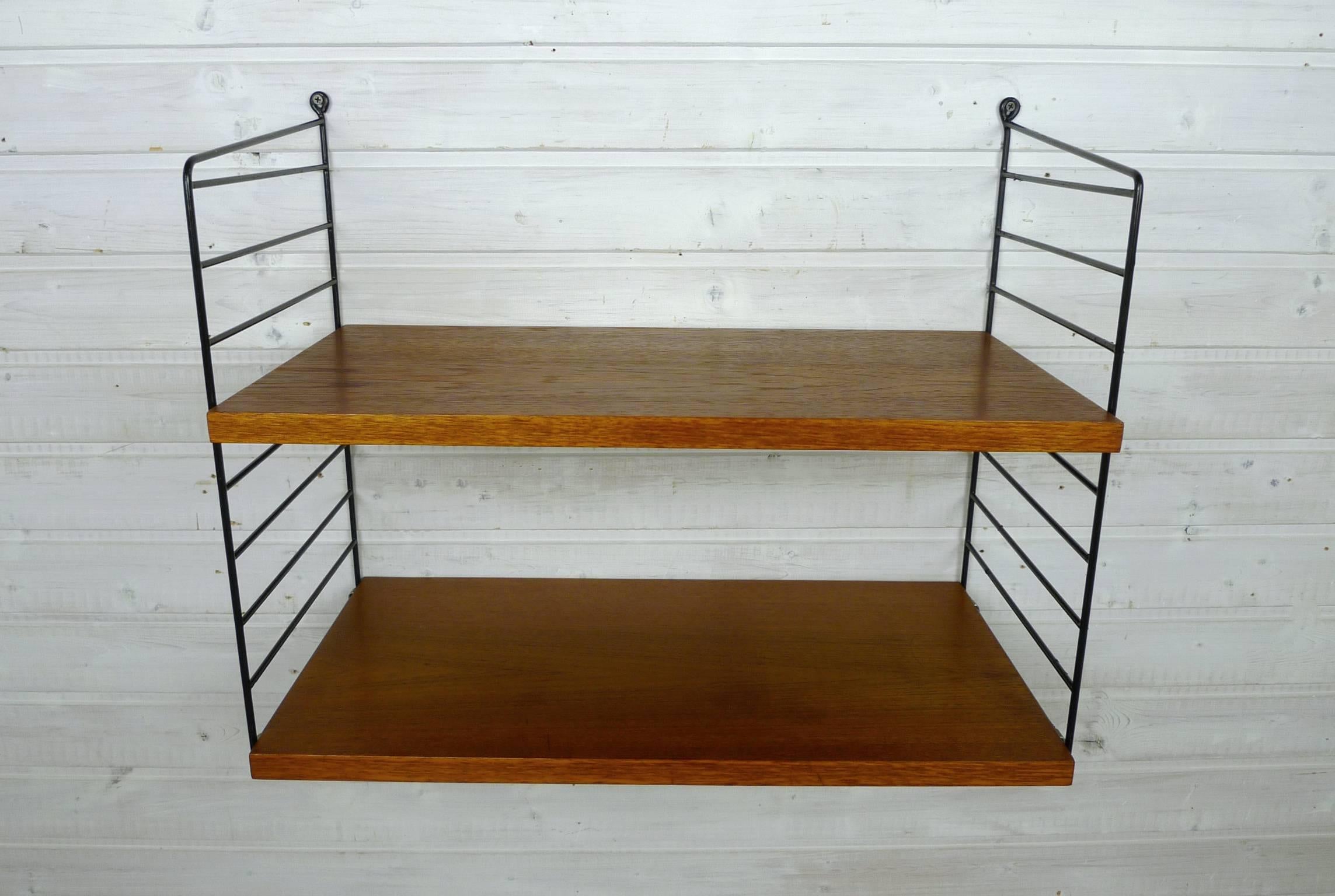 Nisse Strinning designed his famous shelf system in 1949. It was produced in his own company String Design AB in Sweden.
This wall shelf consists of two black-coated ladders and two shelves in teak with a depth of 30 cm. The shelf is in a good