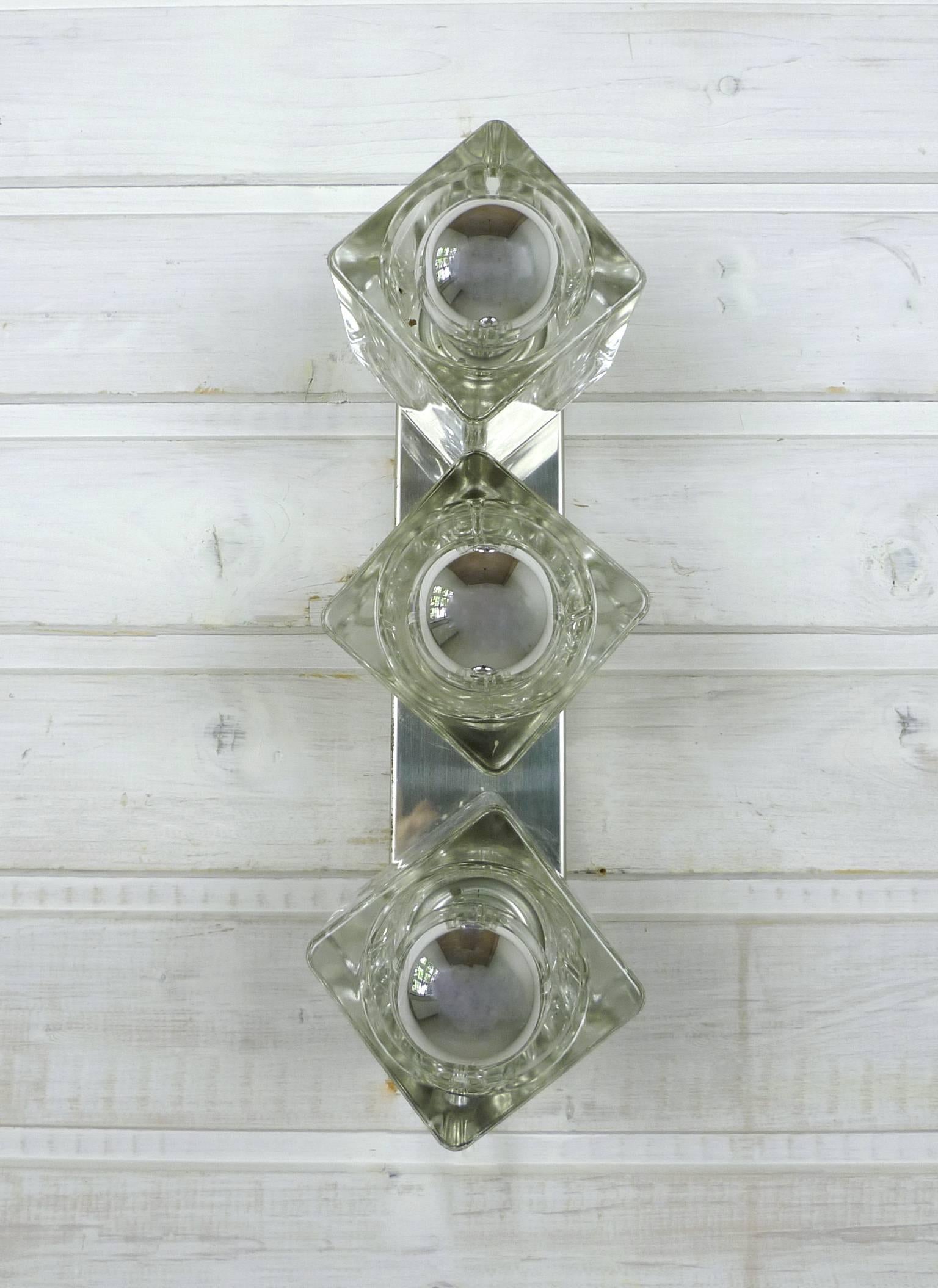 Wall light from the 1970s with three solid glass cubes on a polished metal rail. The wall light can be installed both horizontally and vertically. It is equipped with three E 14 sockets and is in a very good original condition.