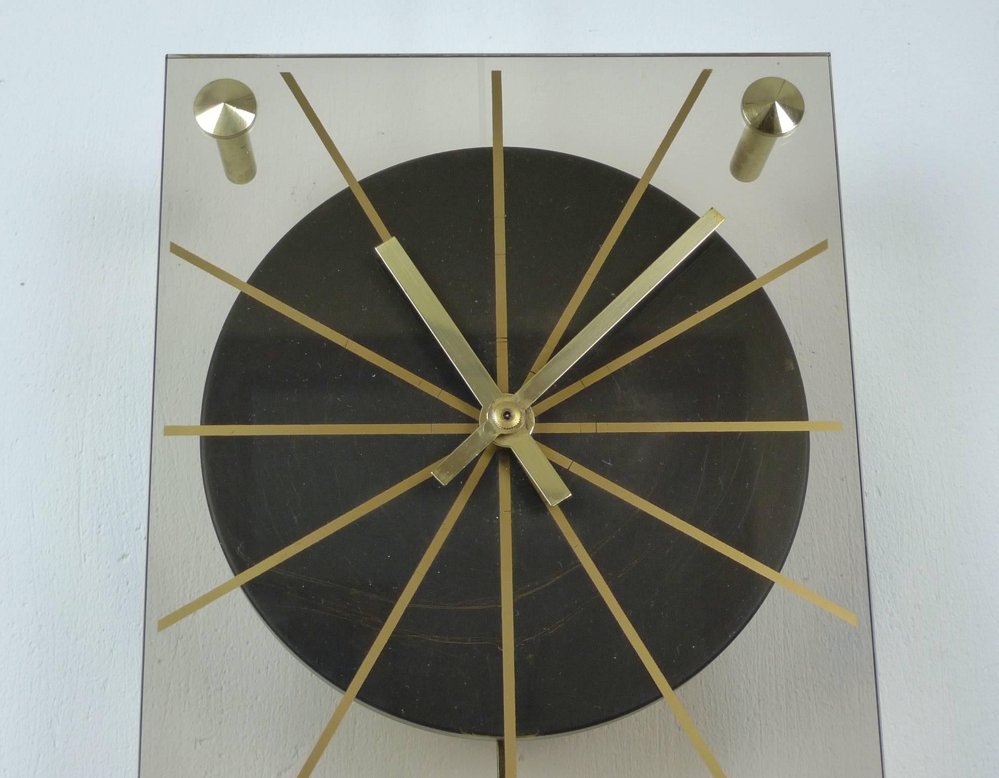 1960s wall clock on tinted Plexiglass with a pendulum bar made of brass. The drive is powered by a battery operated quartz movement from Junghans. This watch is fully functional and is in a very good original condition.