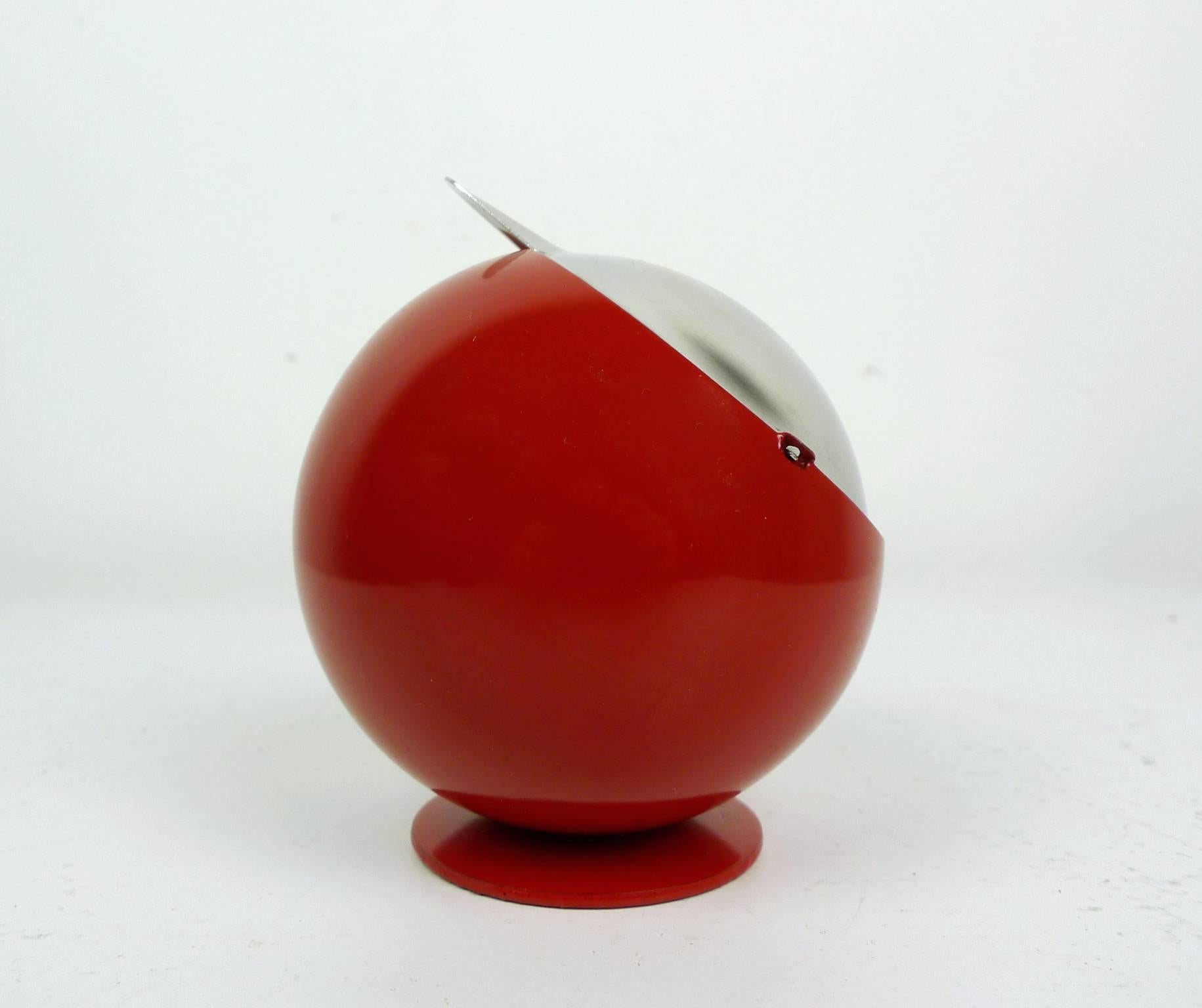 This red metal spherical ashtray with a foldable cigar tray is the Smokny model, developed in the 1970s by the manufacturer F.W. Quist, and produced in Germany. It is in good shape.
