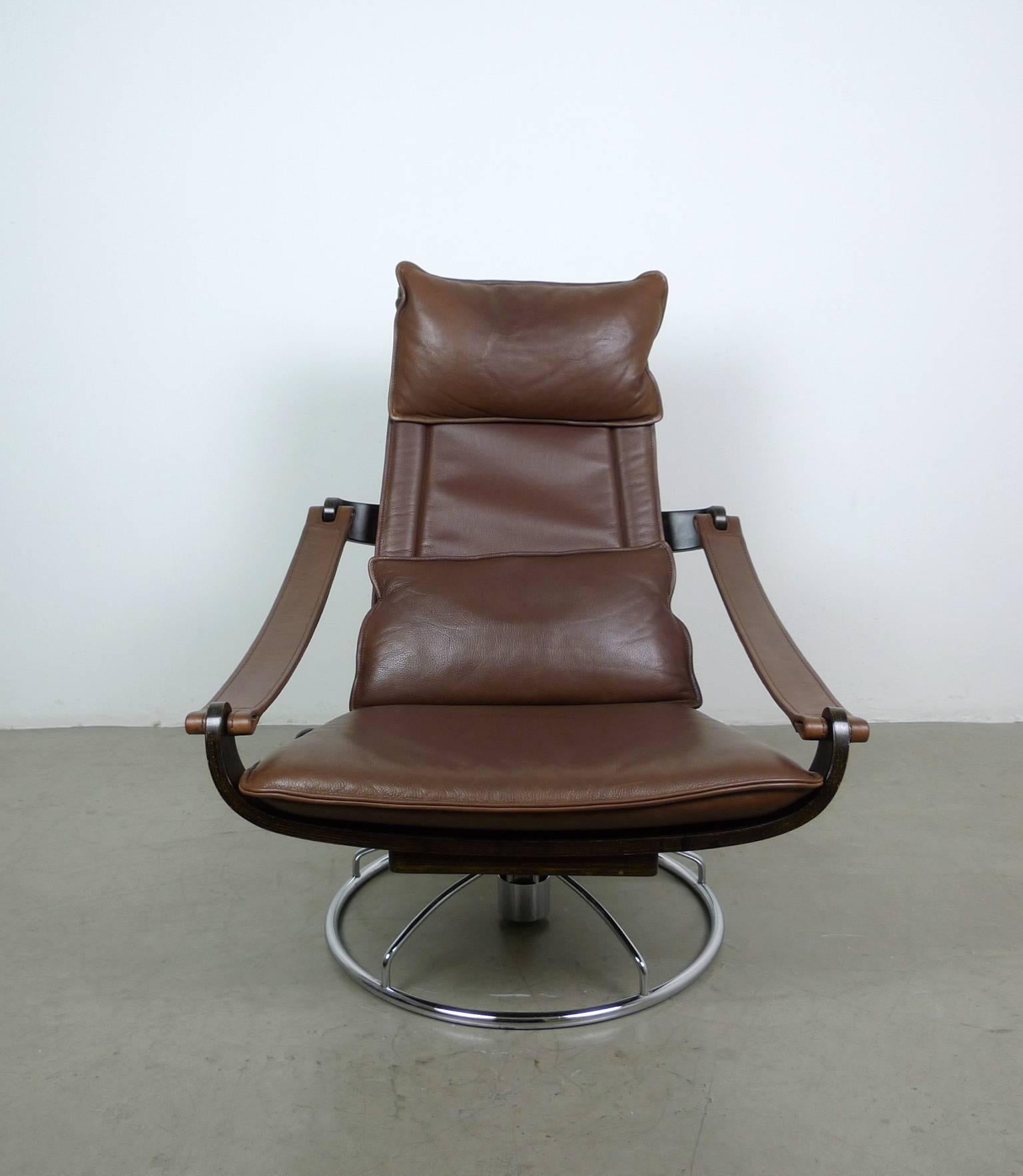 This lounge chair features slim dark brown leather cushions on a chromed swivel base. The frame is composed of individual bent plywood elements. On the right side of the frame is a lever with a large wooden ball, which serves to lock or lower the