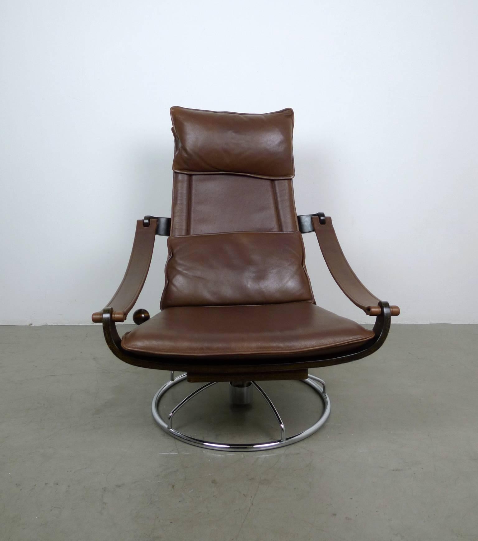 This lounge chair features slim dark brown leather cushions on a chromed swivel base. The frame is composed of individual bent plywood elements. On the right side of the frame is a lever with a large wooden ball, which serves to lock or lower the