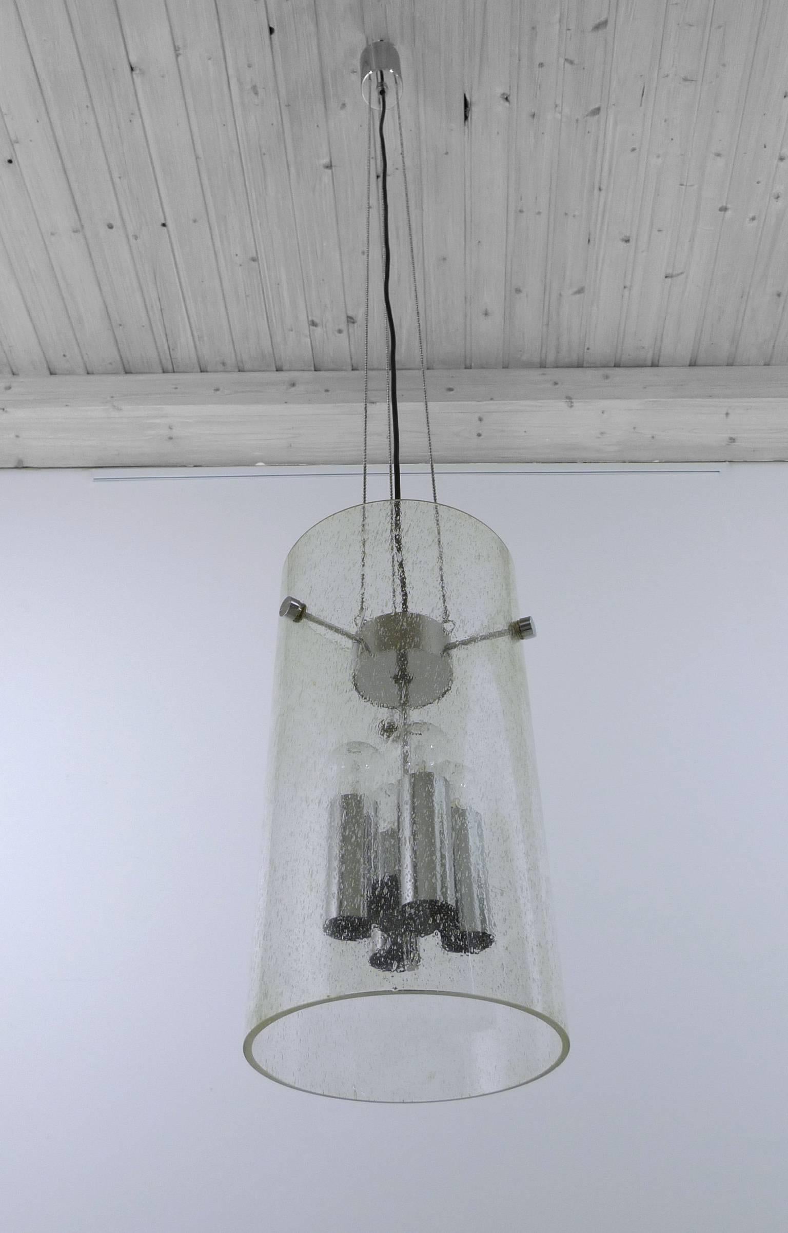 Large cylindrical glass pendant with trapped air bubbles and four E 27 sockets inside. It is suspended from the ceiling by three delicate chains. The glass cylinder has a height of 45 cm. The lamp was produced in the 1970s by Glashütte Limburg in