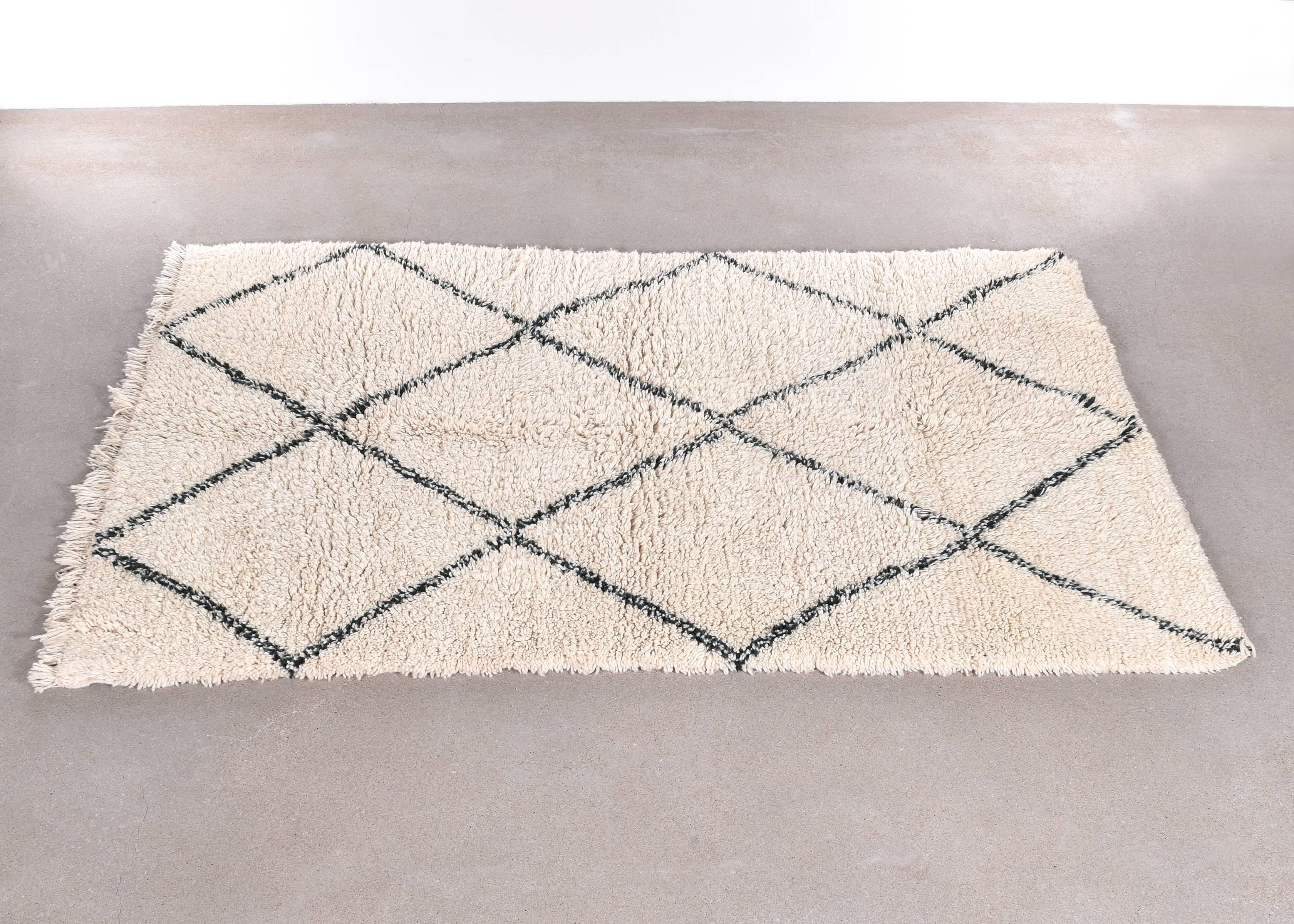 This vintage Beni Ouarain rug is carefully selected in Morocco and has a soft ivory color due to the wool's natural color and are accompanied by dark grey stripes. The rugs are named after the Berber village 'Beni Ouarain' in the Mid-Atlas mountain