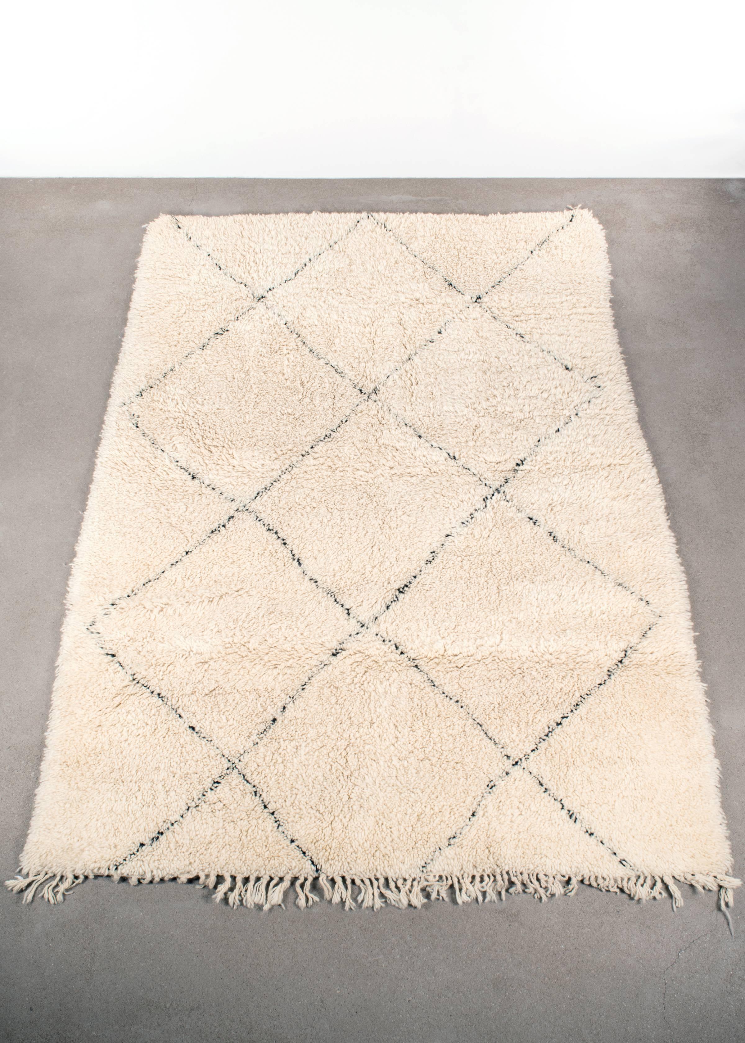 This vintage Beni Ouarain rug is carefully selected in Morocco and has a soft ivory color due to the wool's natural color and are accompanied by dark grey stripes. The rugs are named after the Berber village 'Beni Ouarain' in the mid-atlas mountain