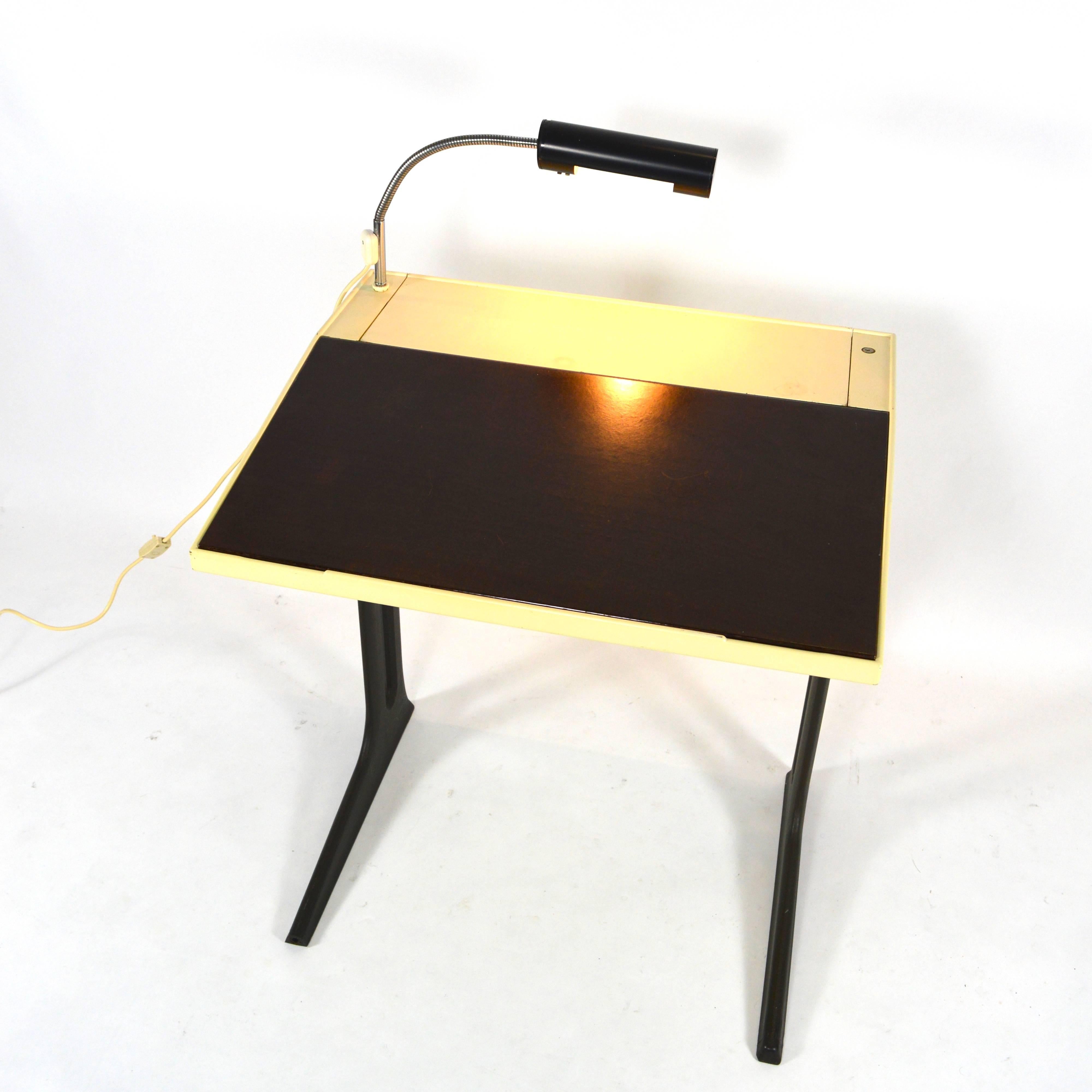 This is a very cool small desk by Elmar Flötotto with rare original lighting.
The brown writing leaf can be lifted to create a straight desk area. The back of the top can be lifted to create a book stand shelve for reading or studying. The desk is