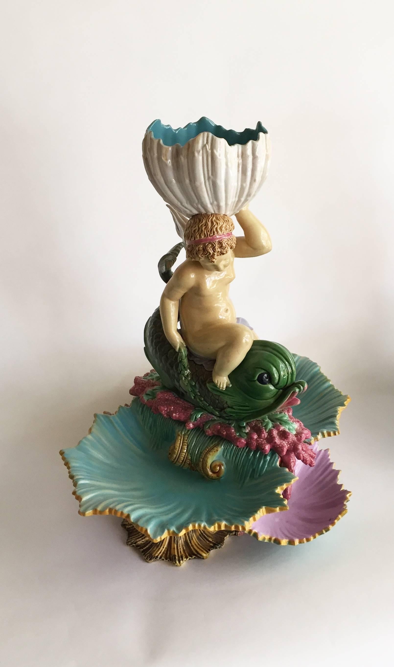 English Victorian George Jones Majolica centerpiece modeled as three shells topped by a putto with a mermaid’s tail to the back, topped by a deep shell serving dish, rendered in rich hues of pink, turquoise, rich green and sea-green, the underside