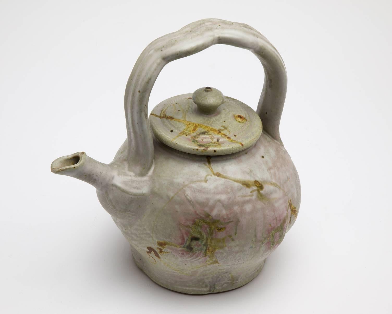 American John Glick studio pottery teapot and cover of globular form with an Asian-inspired arched handle. The teapot body lightly-lobed and decorated with delicate lines and patterns, the body delicately painted with washy brown and pink
