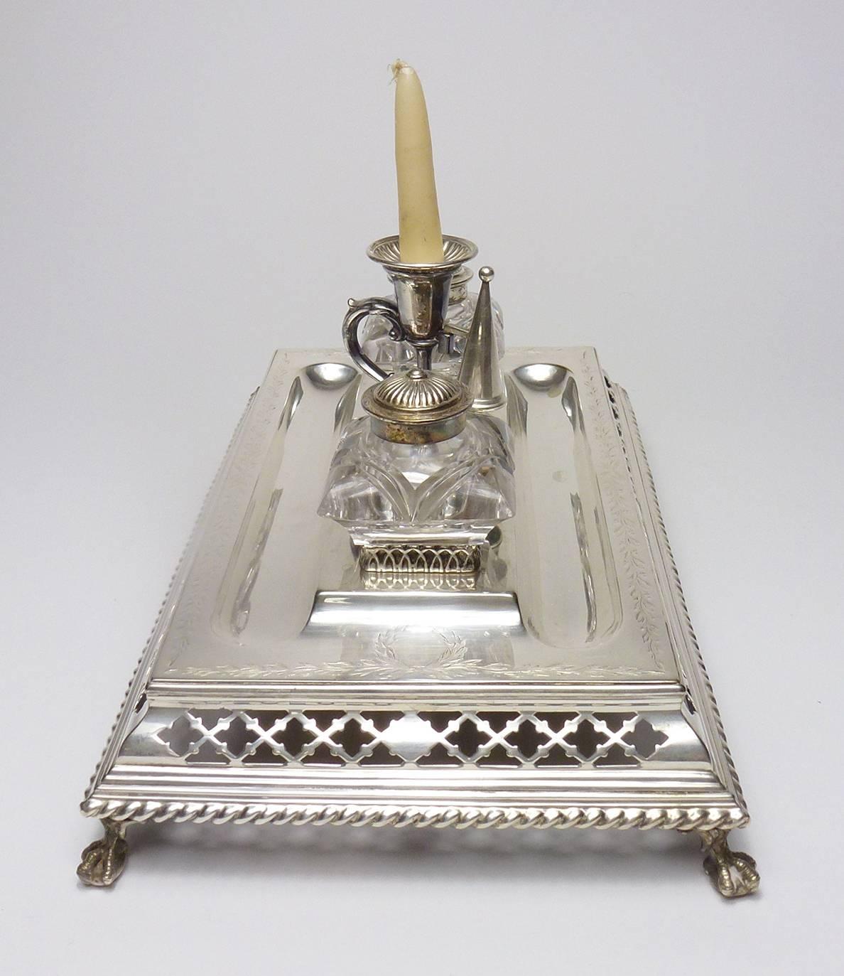 English Victorian Sheffield silver plate Inkstand, the rectangular body with pierced trellis to the stepped body, on four paw feet, with two crystal inkwells with silver caps to the sides of a chamberstick with snuffer. Includes two letter openers