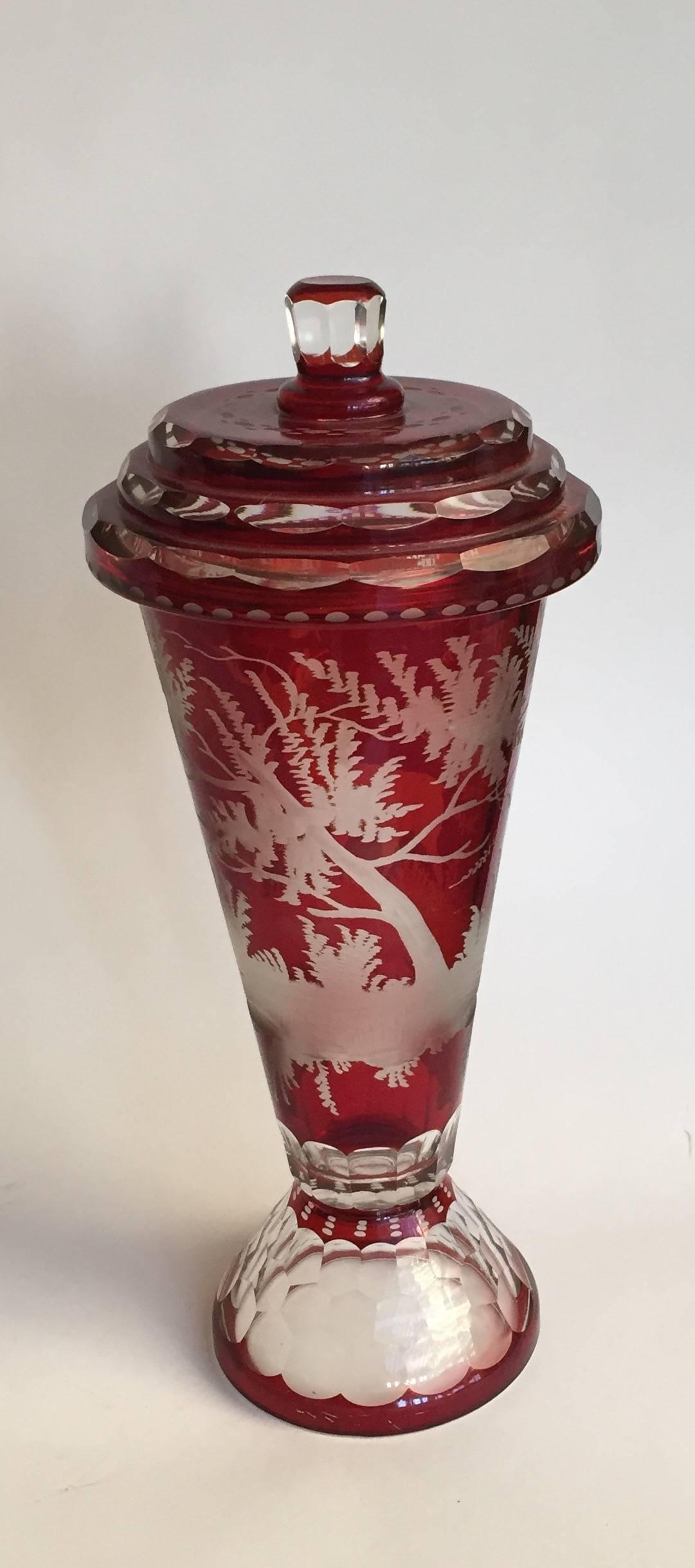 German Czech Bohemian ruby-stained glass covered vase (deckel pokal), the conical vase stained ruby and engraved with a stag or hind or deer in a continuous woodland landscape, the geometric-facetted optic foot above a band of ruby-staining to base.