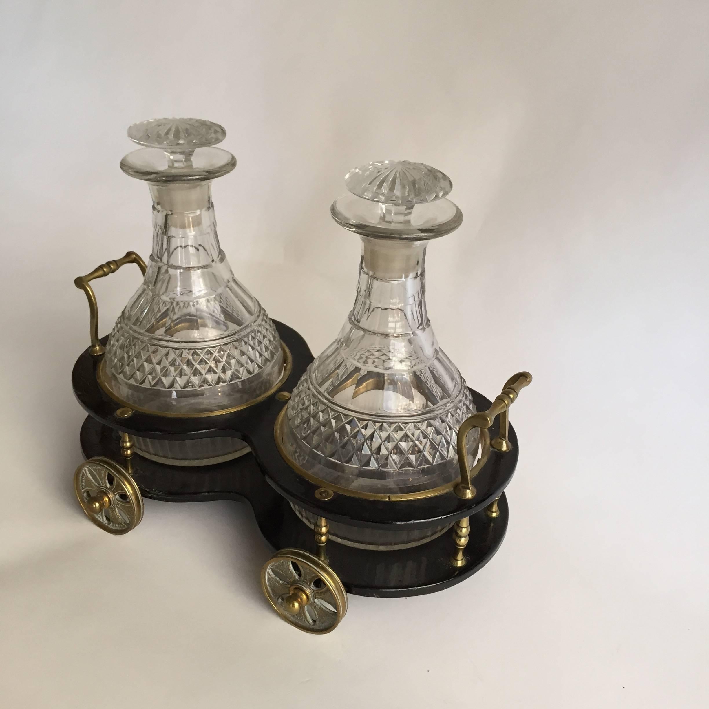 English papier mâché and brass decanter carriage trolleying a pair of Anglo-Irish cut-glass decanters and stoppers. Unmarked, circa 1840. Measures: 5” H., 11 ¼ W. 7 ¼”D., the carriage and the decanters 8 ½” H., 10 1 ¼” HOA. (Minor tiny chips and
