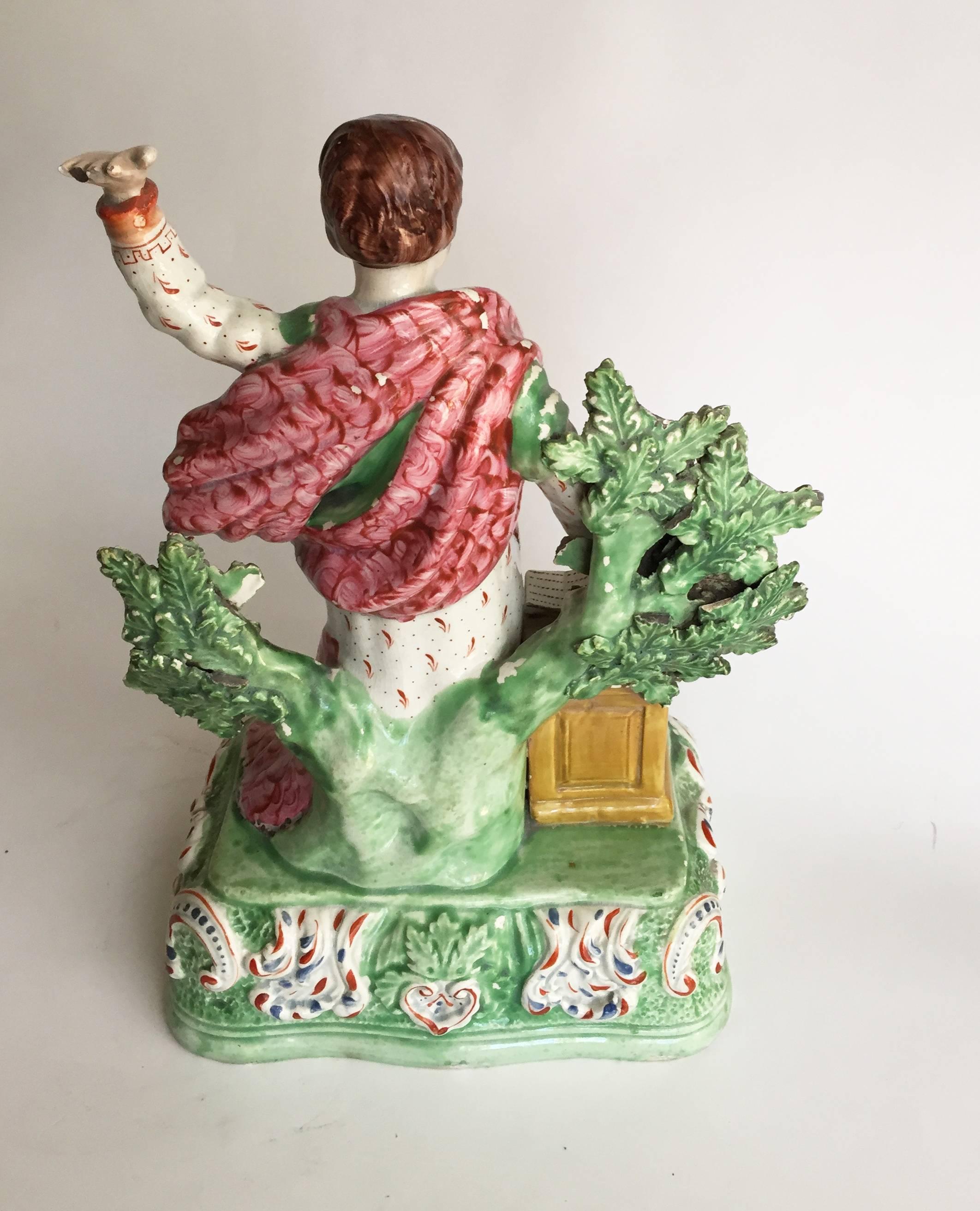 English Staffordshire pottery “Patriotic Group” figure of Jeremiah Preaching, with bocage in the background on a raised, rounded rectangular table base molded with scrolls and foliate patterns, Jesus standing near a large open testament or Bible.