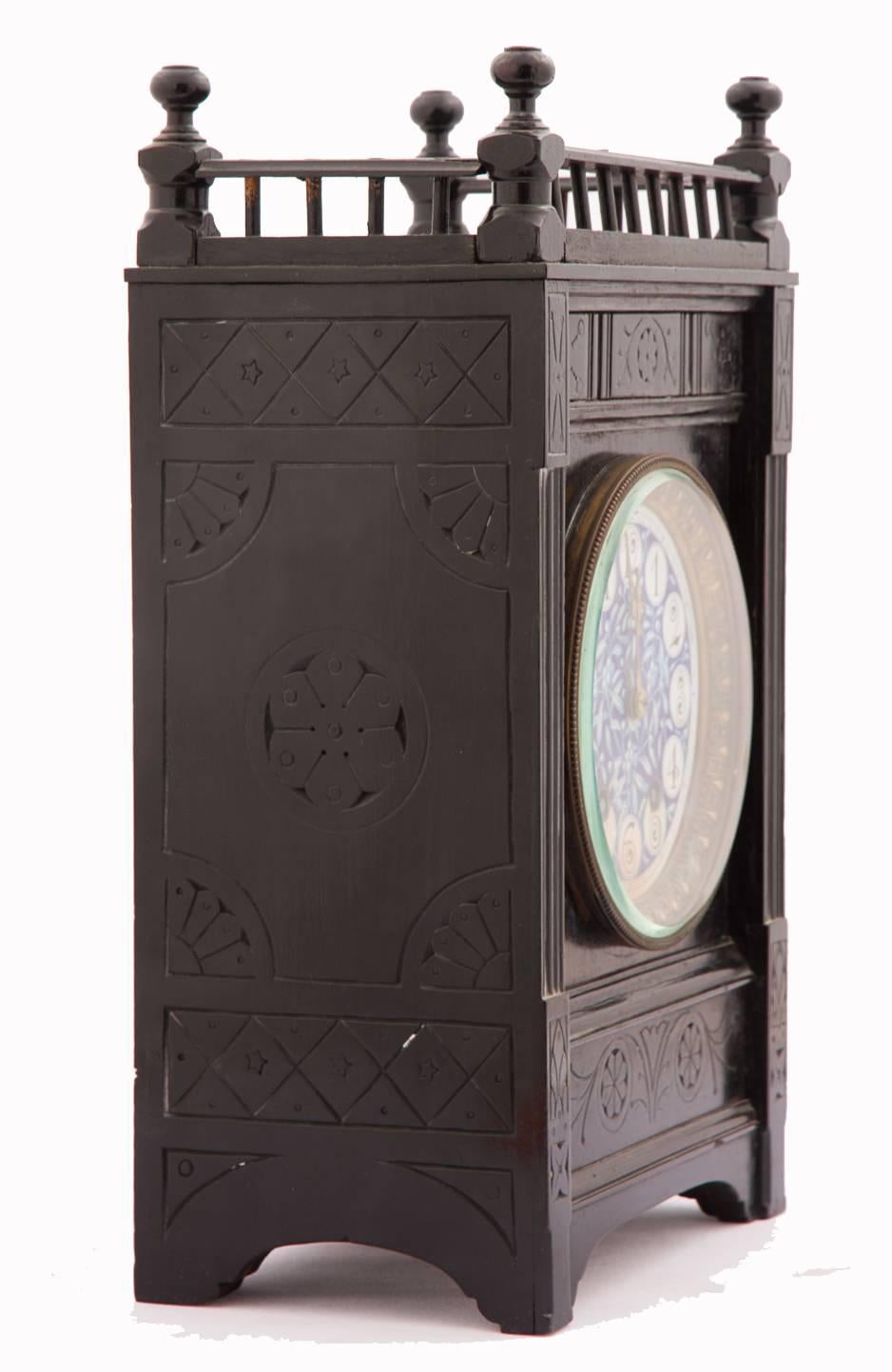 English Aesthetic Movement ebonized wood and pottery mantle clock .

After Lewis F. Day, Attributed to Howell & James, London, of rectangular form, with carved wood gallery above the lightly-carved and incised frame, the rectangular pottery clock