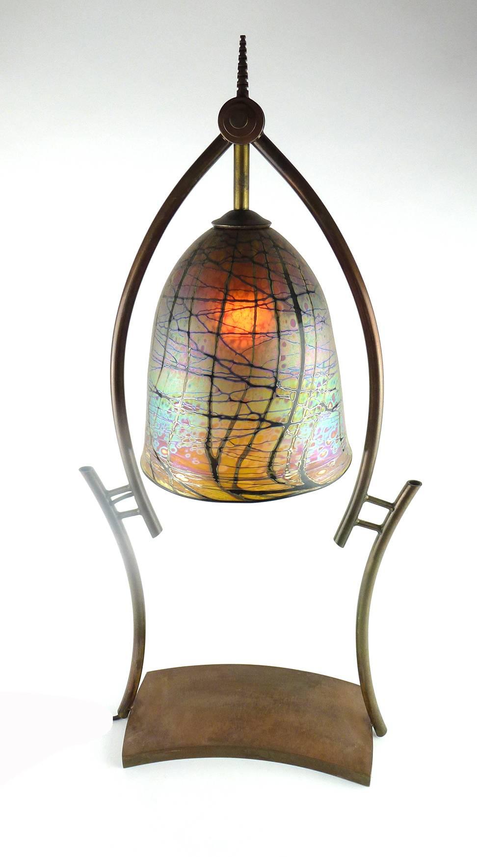 Joe Clearman contemporary Studio Art glass table lamp

Joe Clearman contemporary Studio Art glass table lamp, the shade of gold iridescent glass with metallic enamels and brown-black abstract wraps, pendant from and framed by a copper-finish metal