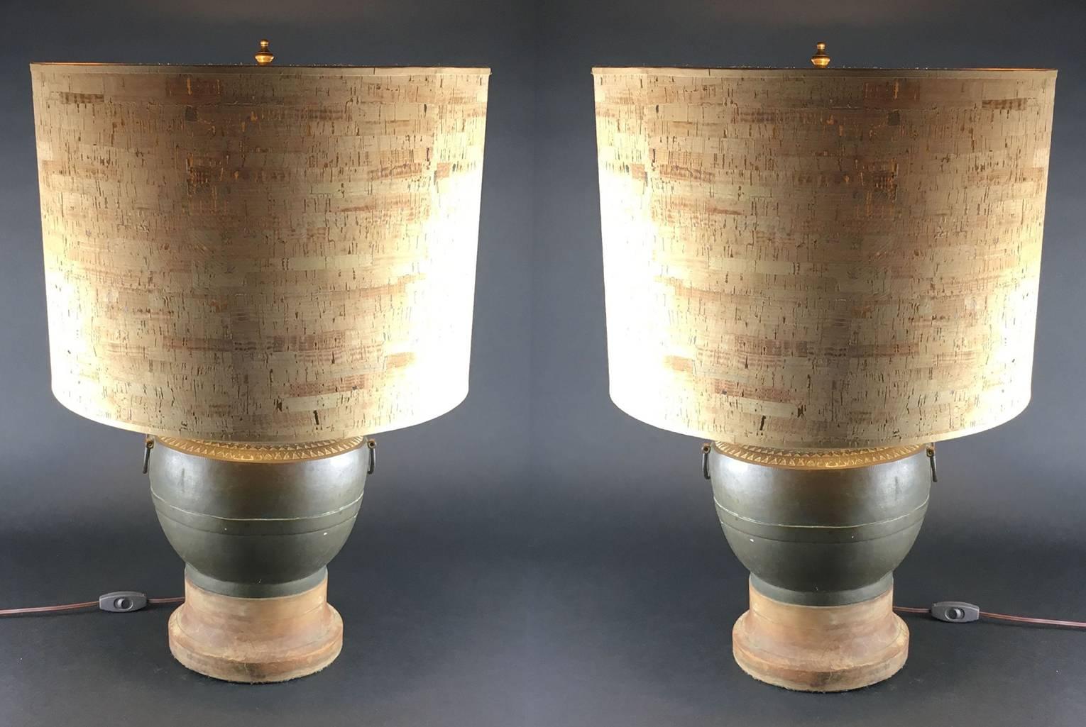 Pair of 1970s metal urn form table lamps with original cork shades, the baluster-form bodies cast with horizontal geometric bands to the shoulders, with rings to the sides. Fitted onto hard-wood bases.

Unmarked. 
Measures: 25