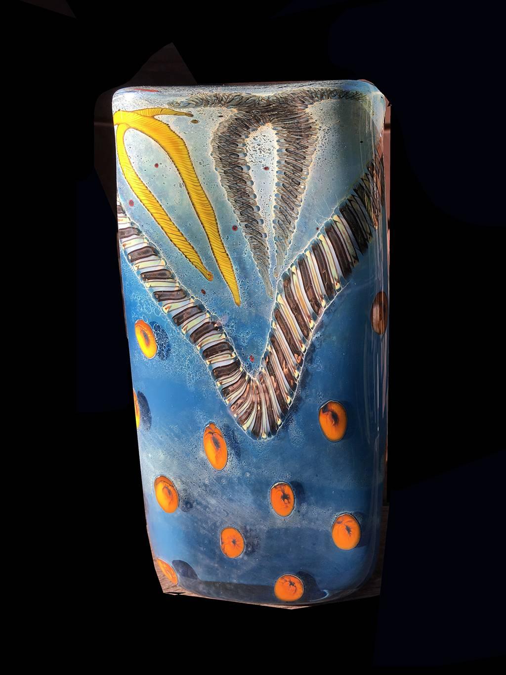 Contemporary studio art glass vase by Kenny Walton 

Contemporary studio glass vase by Kenny Walton (? - 2010), the rectangular vase rendered in various tones of blue, with orange, brown and yellow elements winding along and dotting the