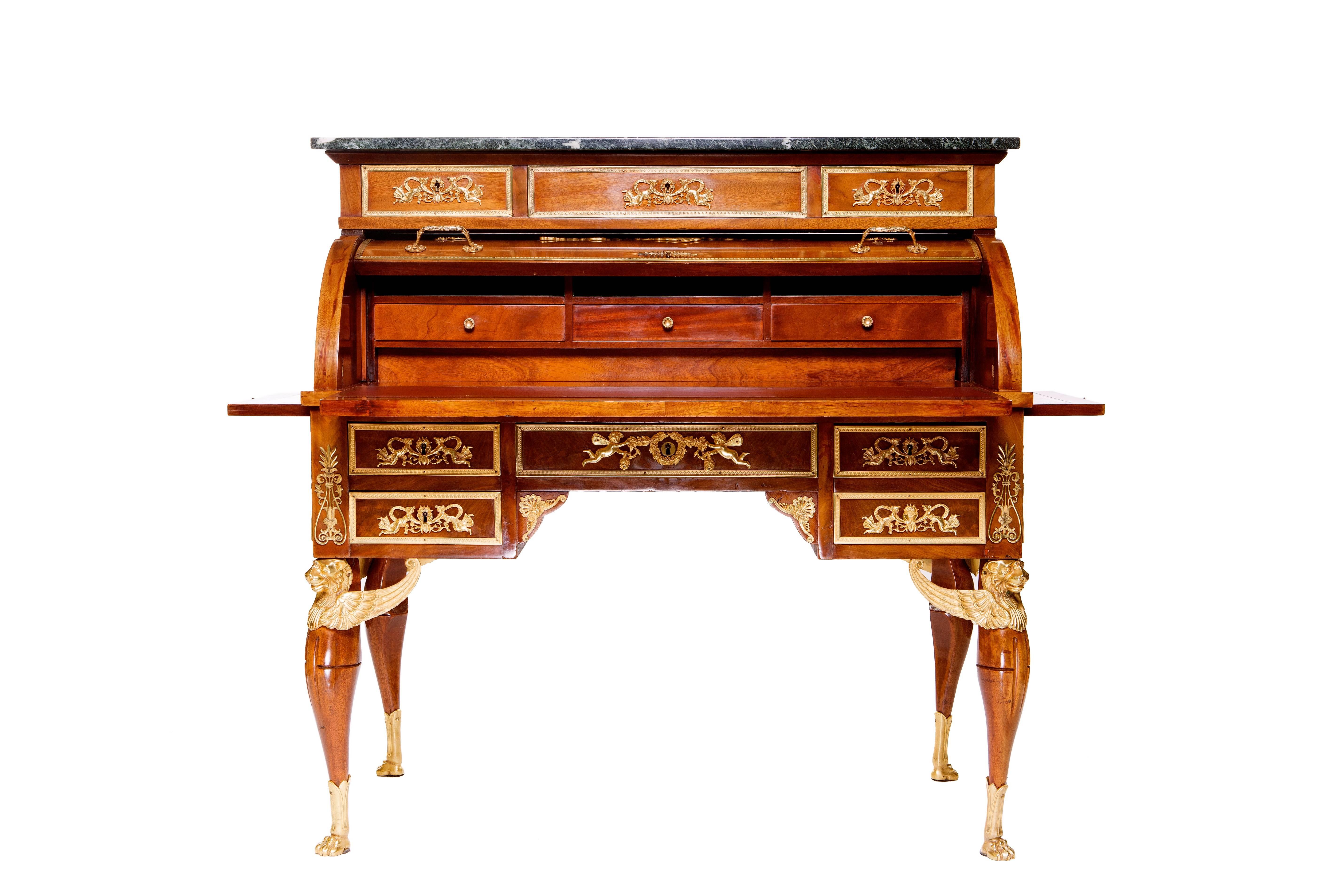 A fine Empire style ormolu-mounted mahogany Cylinder-Bureau. A marble toped rectangular top above one long and two short frieze drawers with ormolu mounts, the cylinder decorated with ormolu mounts on the panel, enclosing three pigeon holes above
