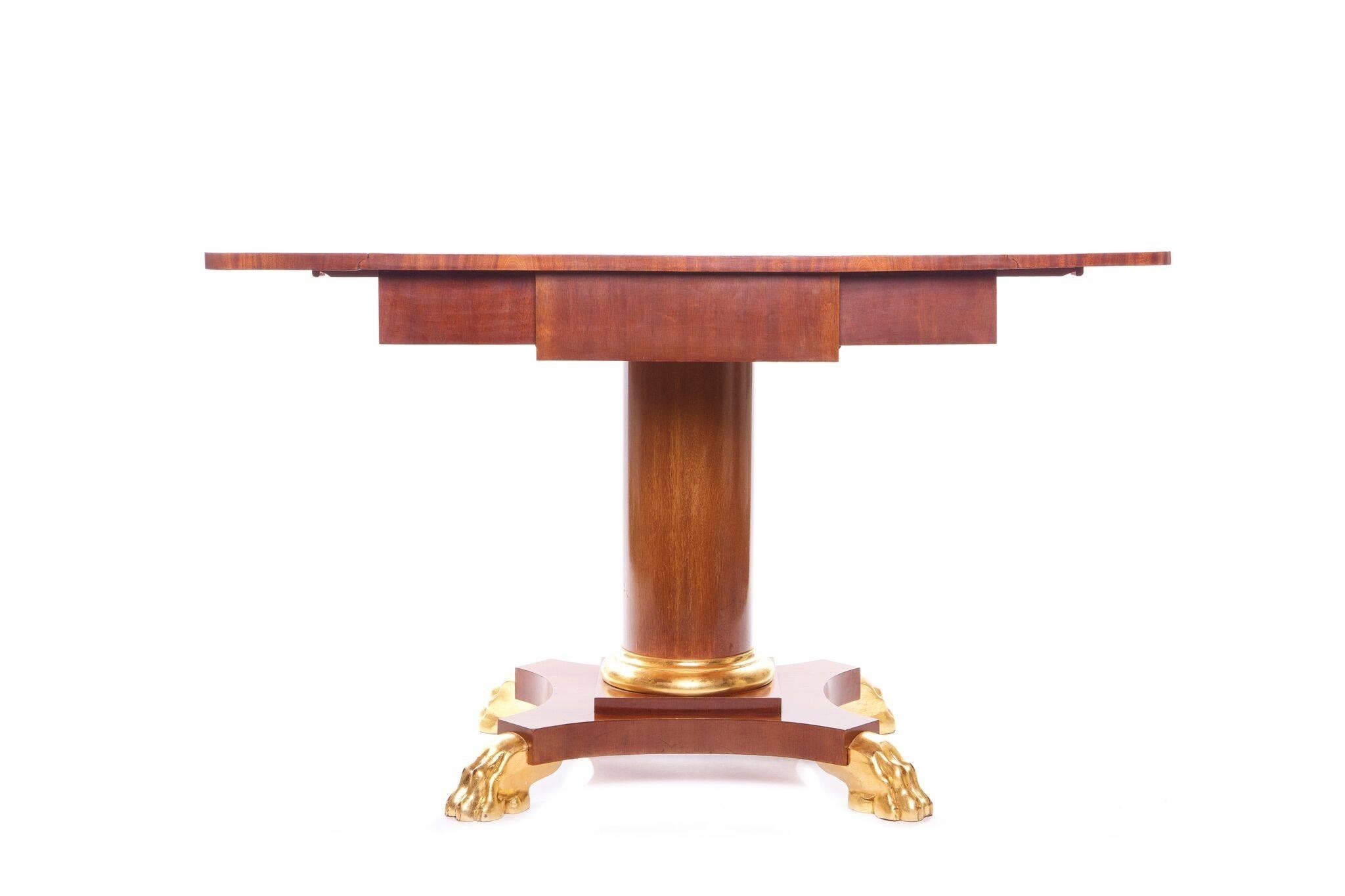 A Danish neoclassical drop-leaf mahogany table with a drawer to the center and drop leaves to the sides, support on a circular center support resting on a shaped base resting on four giltwood lion paws.