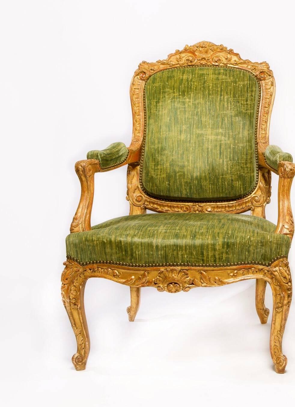 A very fine pair of large Louis XV style gilt-wood Fauteuils En Cabriolet of richly carved details with a cartouche-shaped leaf-carved backrest, the serpentine top rail center by a shell and foliate motif, the padded armrest raised on voluted