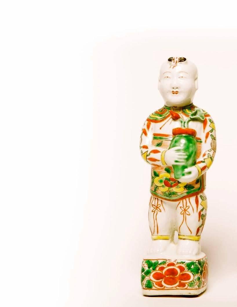 A pair of Chinese Famille Verte porcelain Hoho figures of boys holding pot with Lotus flowers on stands, decorated in the Fammille Verte style.