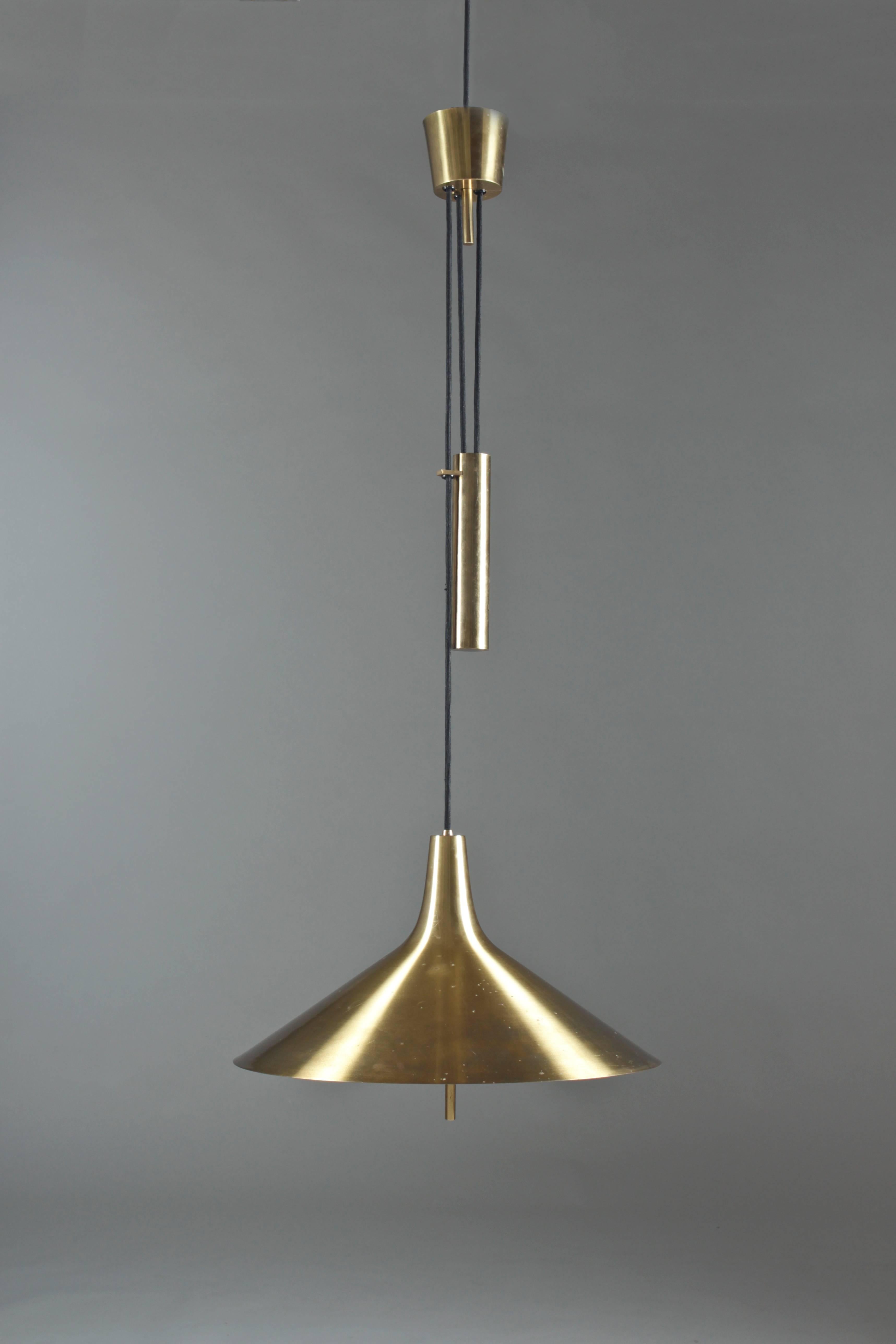 Stunning pendant in brass with adjustable height. The lamp features a black fabric wire connected to a solid brass weight and canopy. The brass shows beautiful patina.