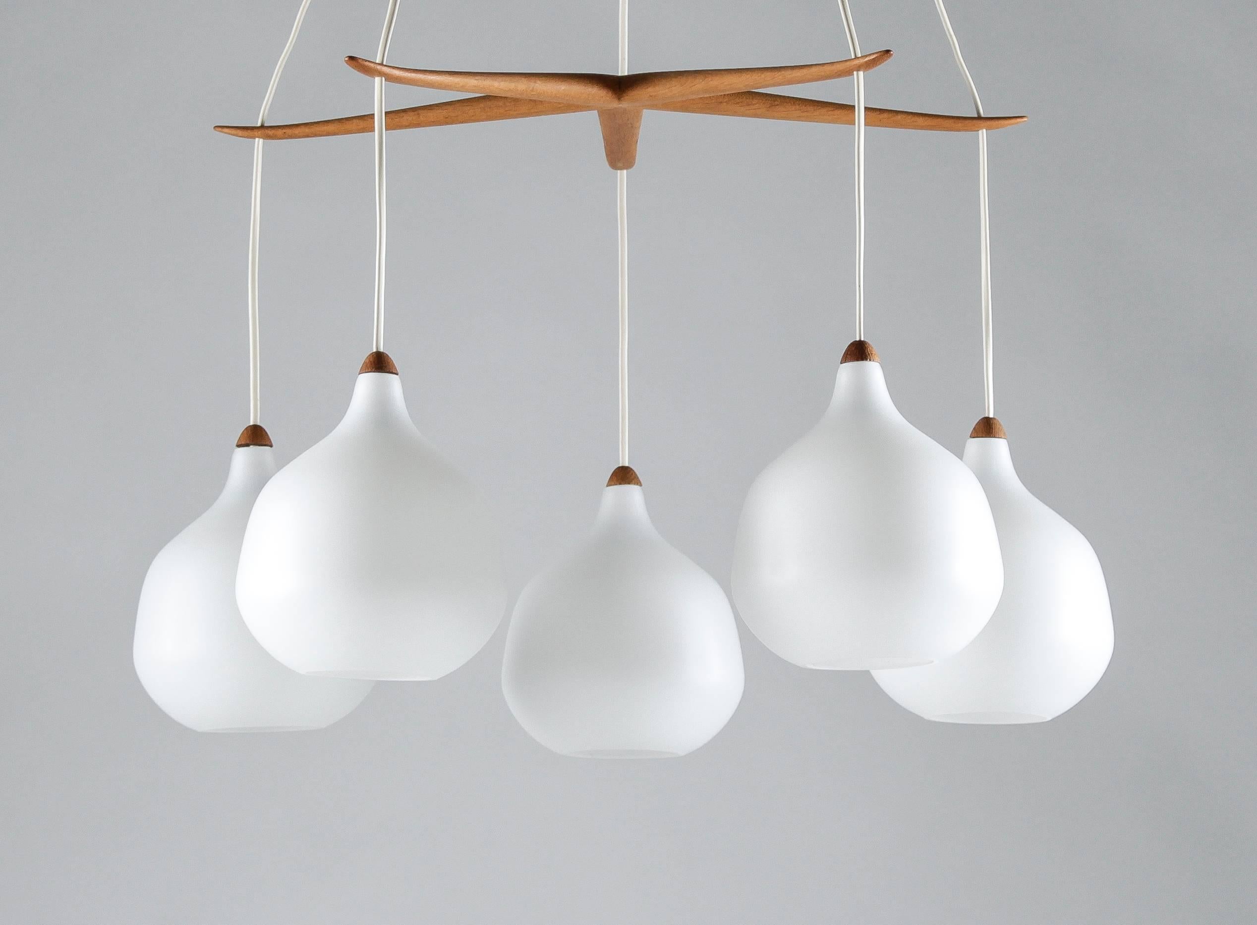 Rare chandeliers by Uno & Osten Kristiansson for Luxus. The chandeliers feature five opaline glass globes, separated by an elegant star-shaped divider in oak, which can be moved to adjust the height of the globes. The frosted opaline glass gives a