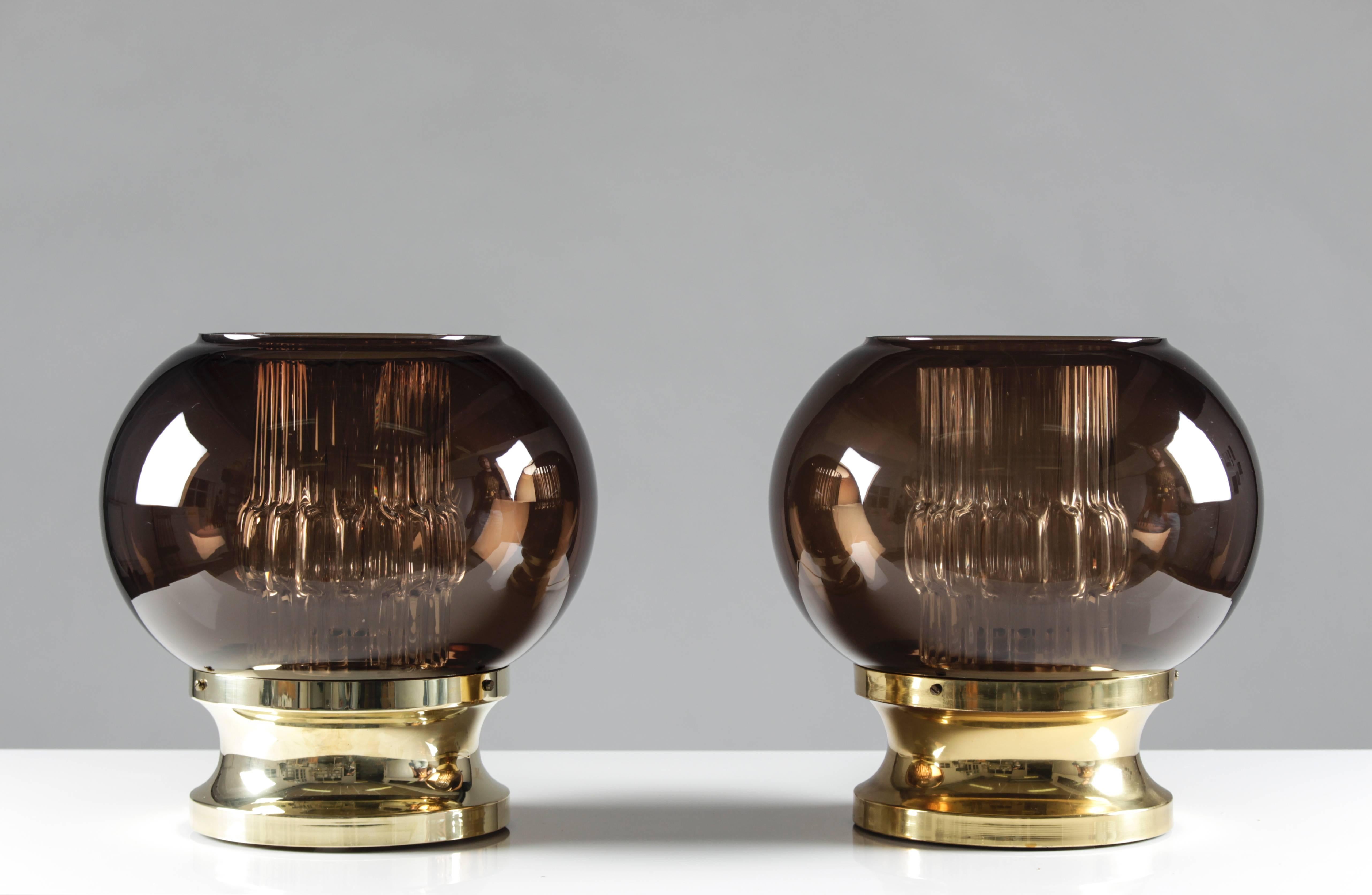 A pair of table lamps made by Carl Fagerlund for Orrefors. The lamps feature a brass base, holding two glass shades; one cylinder-shaped in clear glass and a bigger globe in brown/violet glass. There is an ever so slight nuance in color in the brass