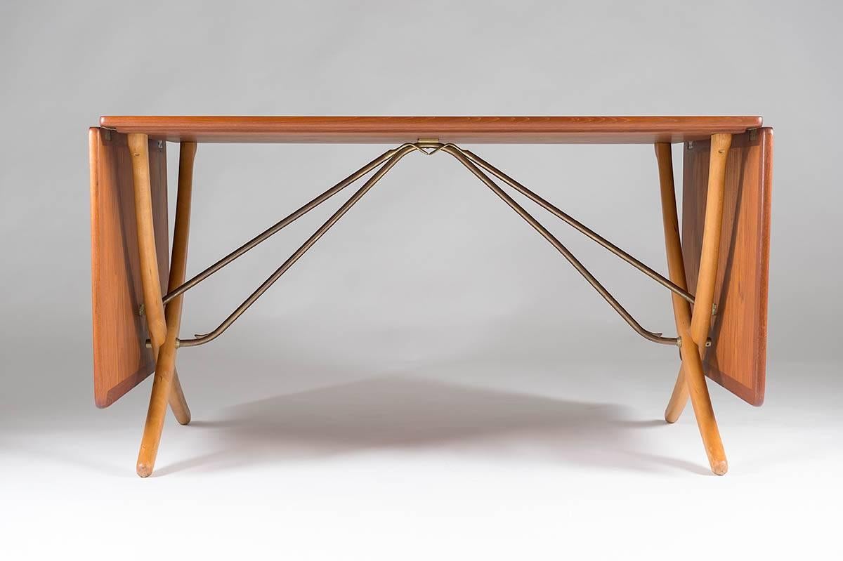 Rare drop-leaf table AT-304 by Hans J. Wegner for Andreas Tuck. This stunning dining table is made of teak with legs of birch. The drop leaves are held by brass rods that lock automatically when you pull up the leaves; function and design in true