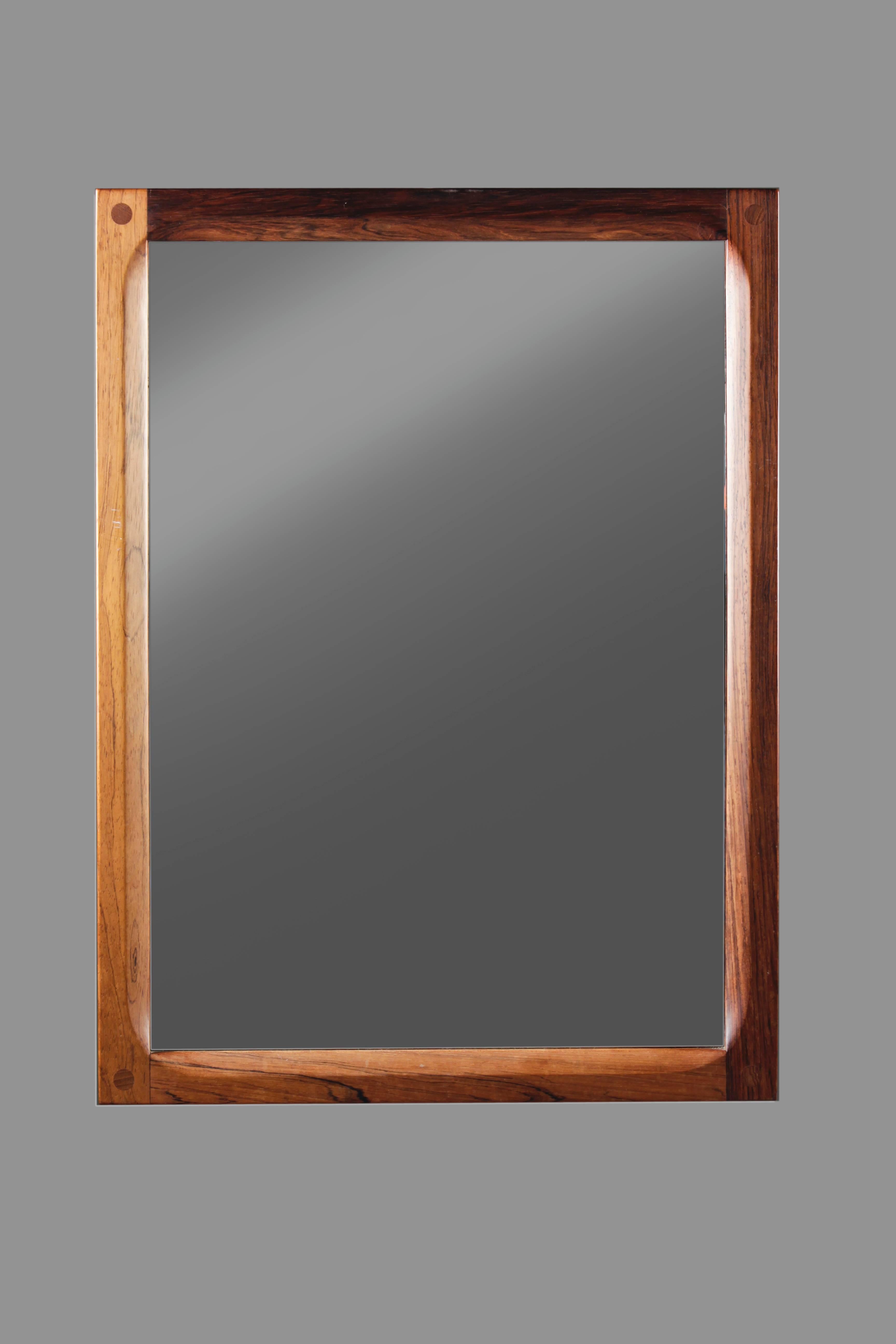 Wall mirror with a beautifully carved frame in rosewood by Danish designer Aksel Kjersgaard.
On the photographs the difference in the color of the wood seems very big. In 