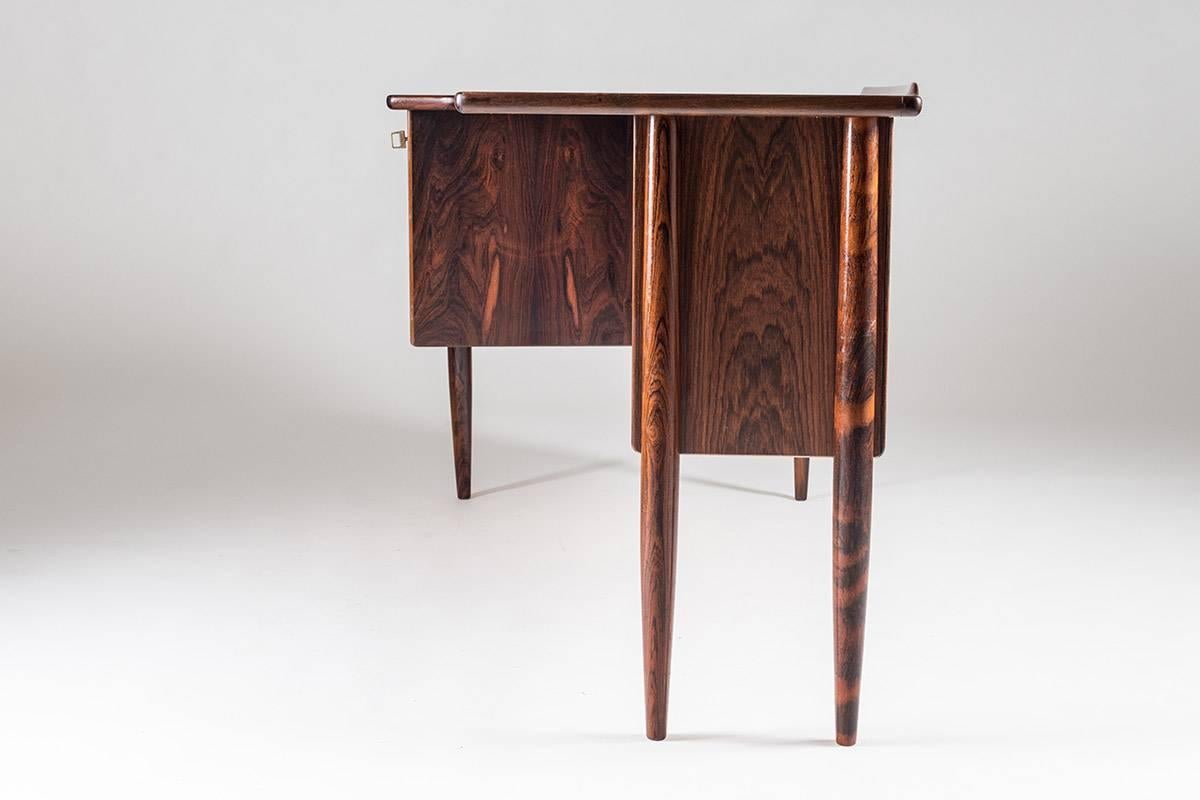 A desk in rosewood by Göran Strand for Lelångs Möbelfabrik, Sweden 1950s. This asymmetric shaped desk shows beautiful details and great build quality. In the front you find three drawers with beautiful shaped handles and a lock on the upper drawer.