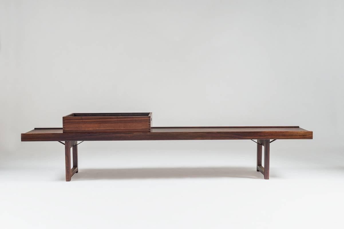 Krobo bench in rosewood by Torbjørn Afdal for Mellemstrand, Norway, with flower or magazine box.
This beautiful piece is made of solid wood with thick rosewood veneer with beautiful grain. It can be used as a bench, coffee table, or even to put